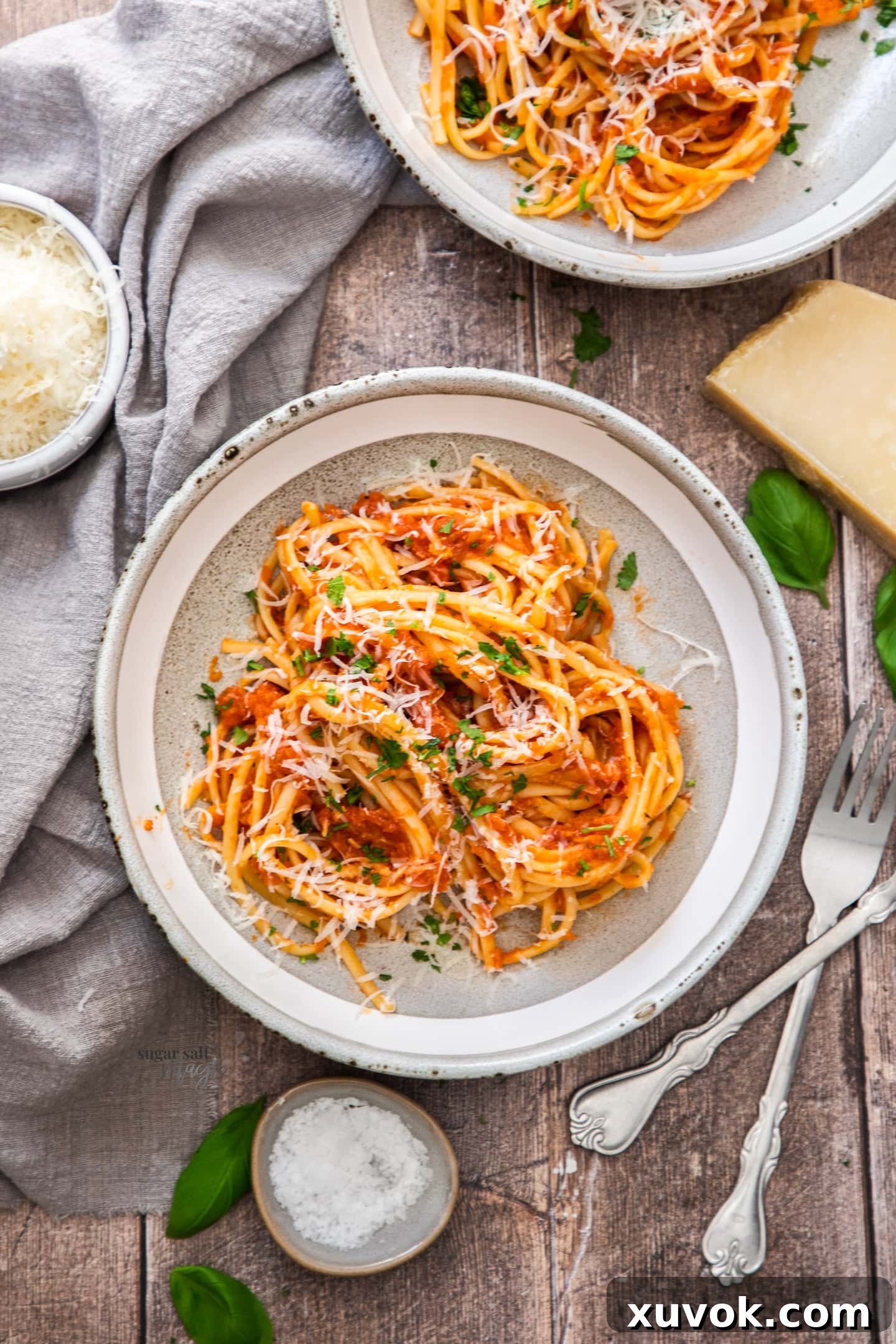 A top-down view of a single, perfectly plated bowl of Pasta Napoletana. The spaghetti is expertly twirled onto a fork, garnished with vibrant fresh basil leaves and a dusting of grated Parmesan cheese, resting invitingly on a wooden table, emphasizing its deliciousness and readiness to be savored.