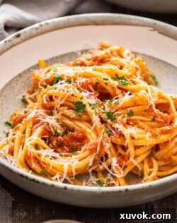 Closeup of Pasta Napoletana in a bowl, showing the rich tomato sauce coating the spaghetti and garnished with fresh basil and Parmesan.
