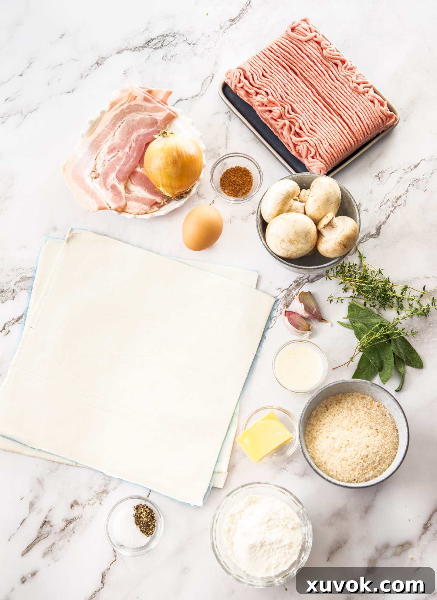 A selection of fresh ingredients for making turkey sausage rolls laid out on a marble surface.