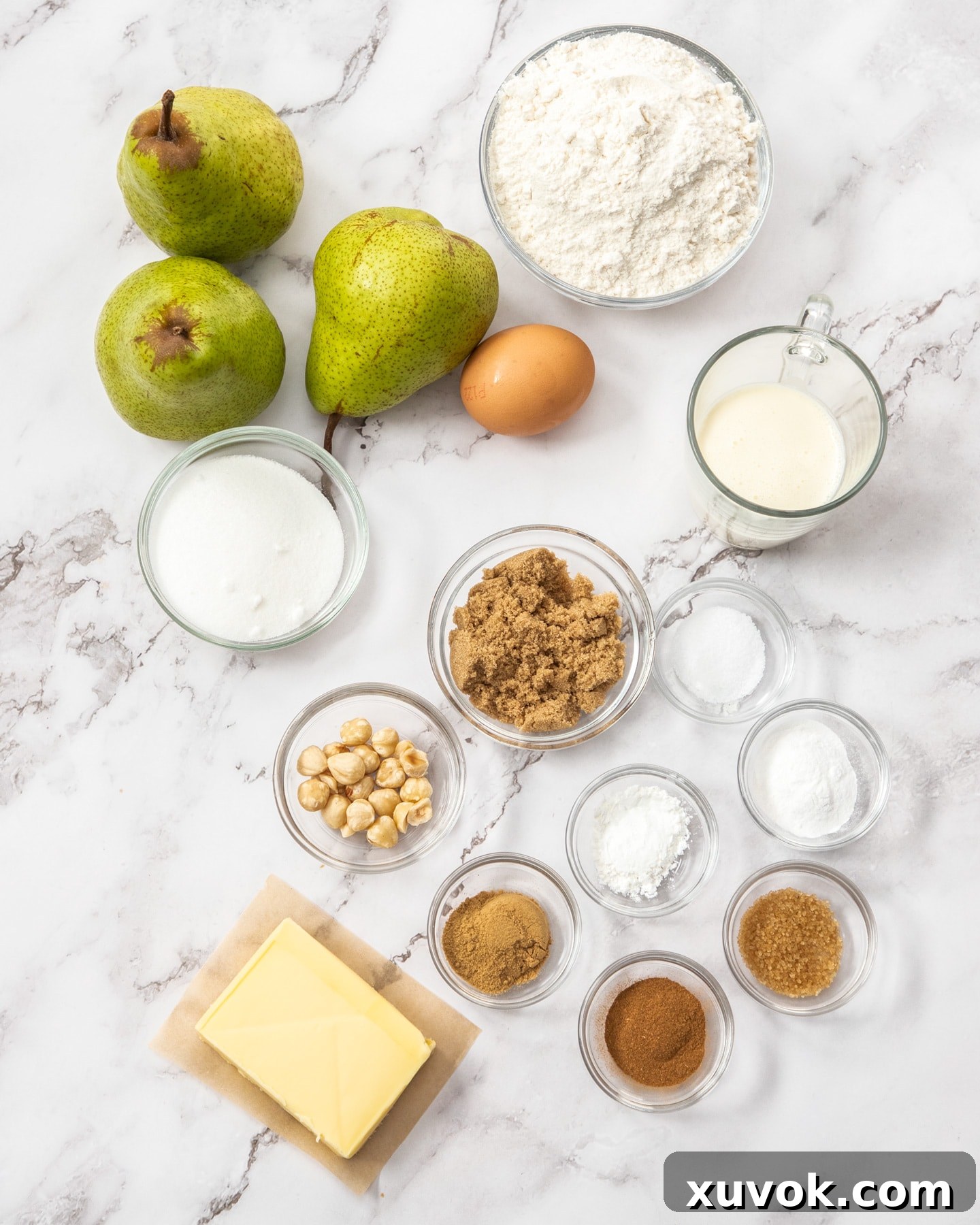Ingredients for fresh pear cobbler laid out on a marble surface, including pears, butter, sugar, flour, and spices.