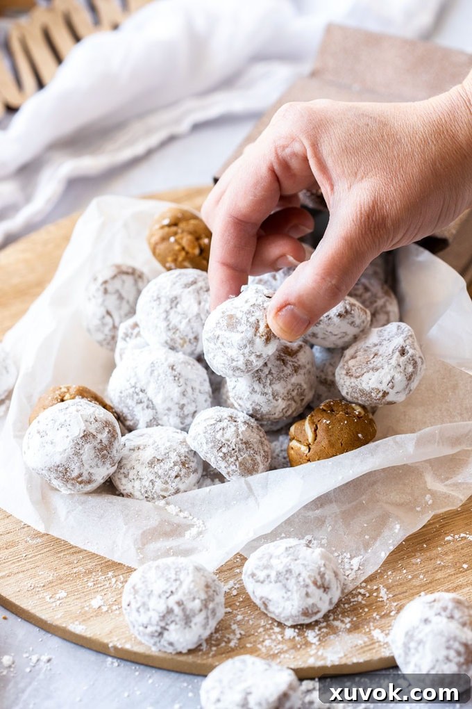A hand reaching in to grab a gingerbread snowball cookie that has tumbled out of a gift bag, showcasing its powdered sugar coating.