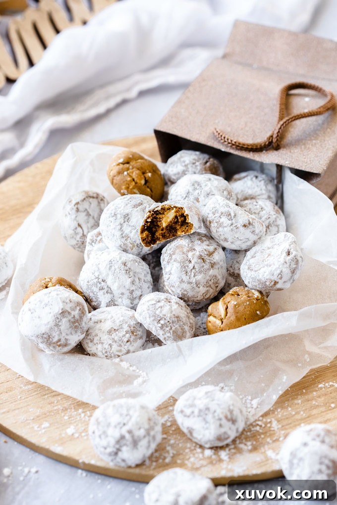 A festive arrangement of gingerbread flavored snowball cookies, elegantly tumbling out of a gift bag onto a pristine piece of white baking paper.