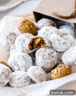 A pile of gingerbread flavoured snowball cookies, tumbling out of a gift bag onto a piece of white baking paper
