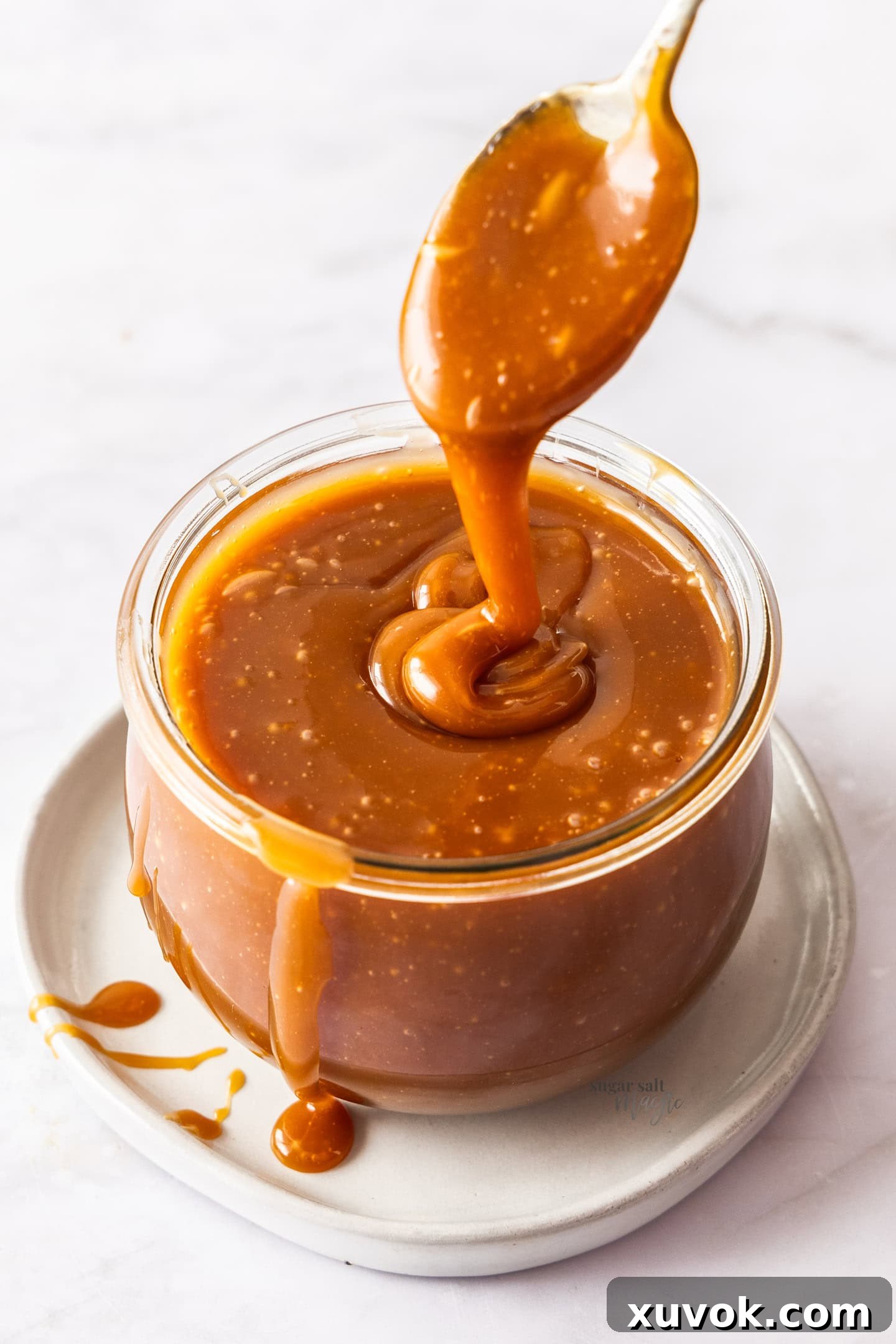 Caramel sauce slowly drizzling from a spoon into a jar. A perfect homemade caramel sauce.