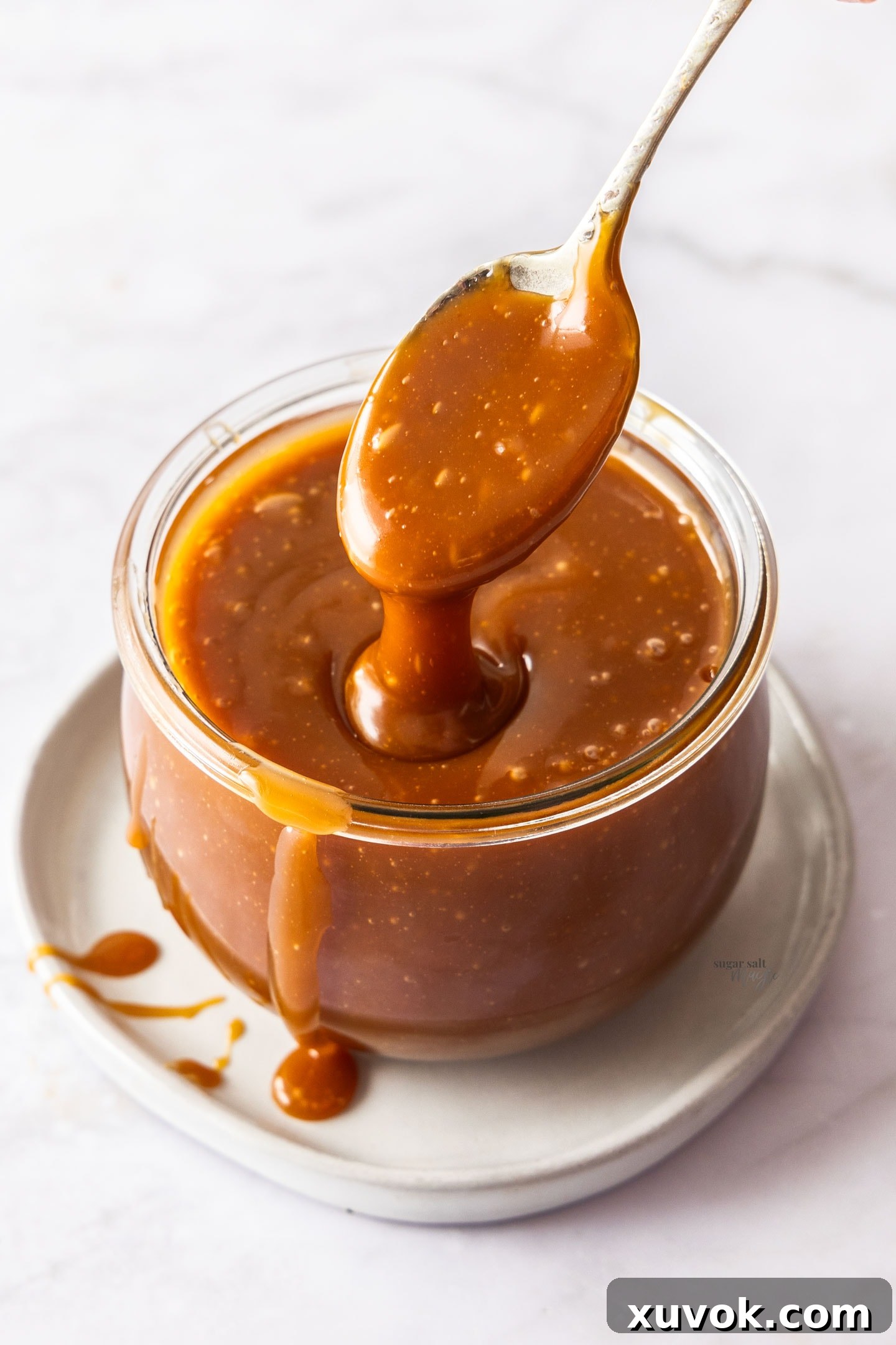 A spoon taking a generous scoop of homemade caramel sauce out of a jar, ready to be enjoyed.