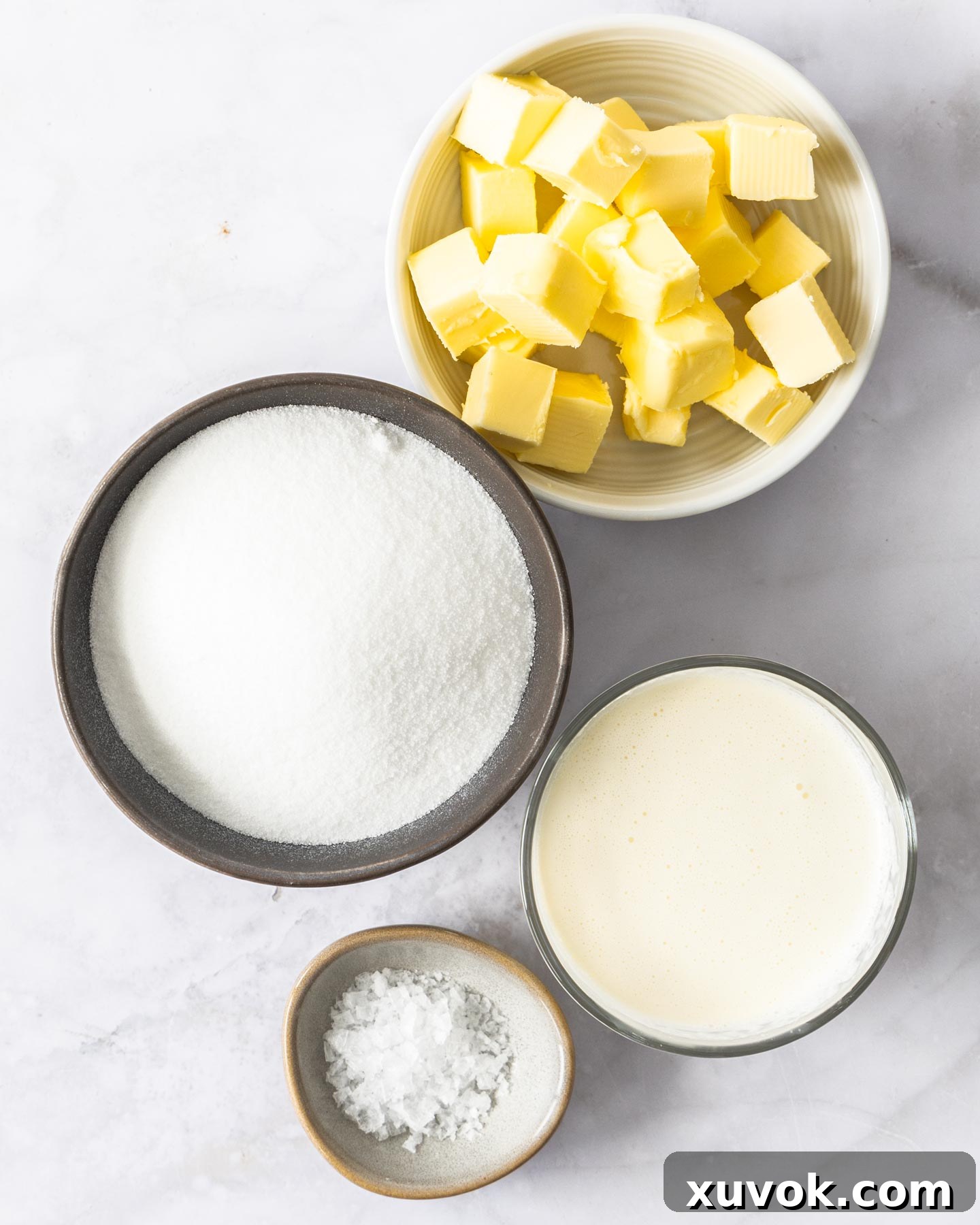 Ingredients for homemade caramel sauce laid out: sugar, cream, butter, and sea salt flakes.