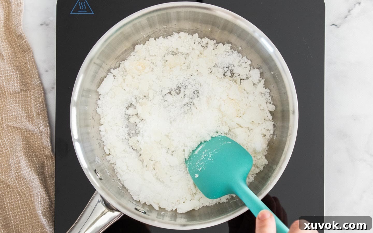 Sugar granules just starting to clump and melt in a stainless steel pan, indicating the beginning stage of caramelization.