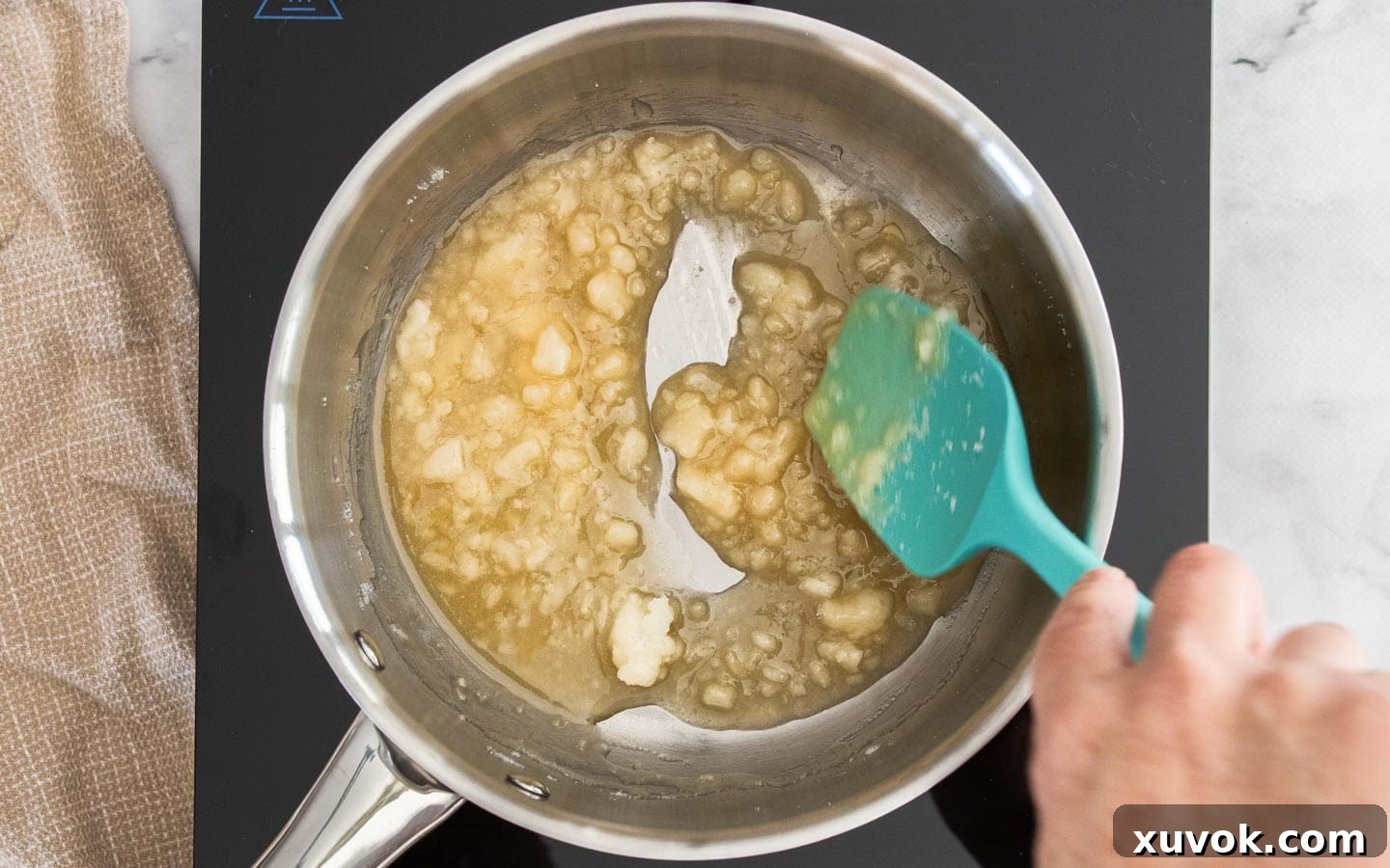 Sugar clumps in a pan, about halfway melted, with some liquid golden caramel forming around the edges.