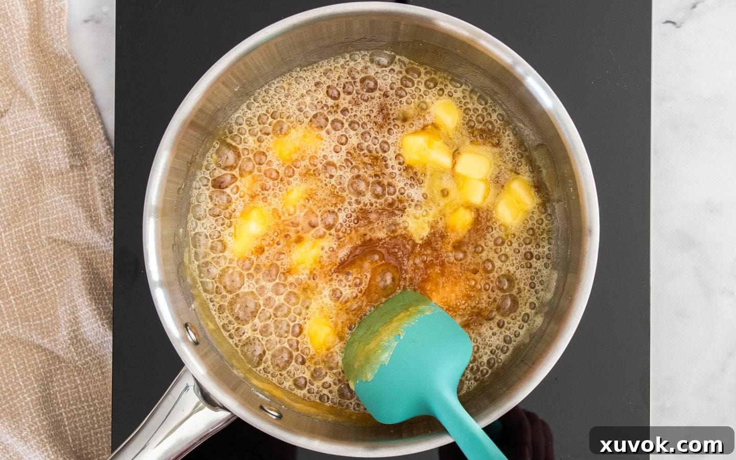 Cubed butter melting into the hot, amber caramel in the pan, creating a rich mixture.