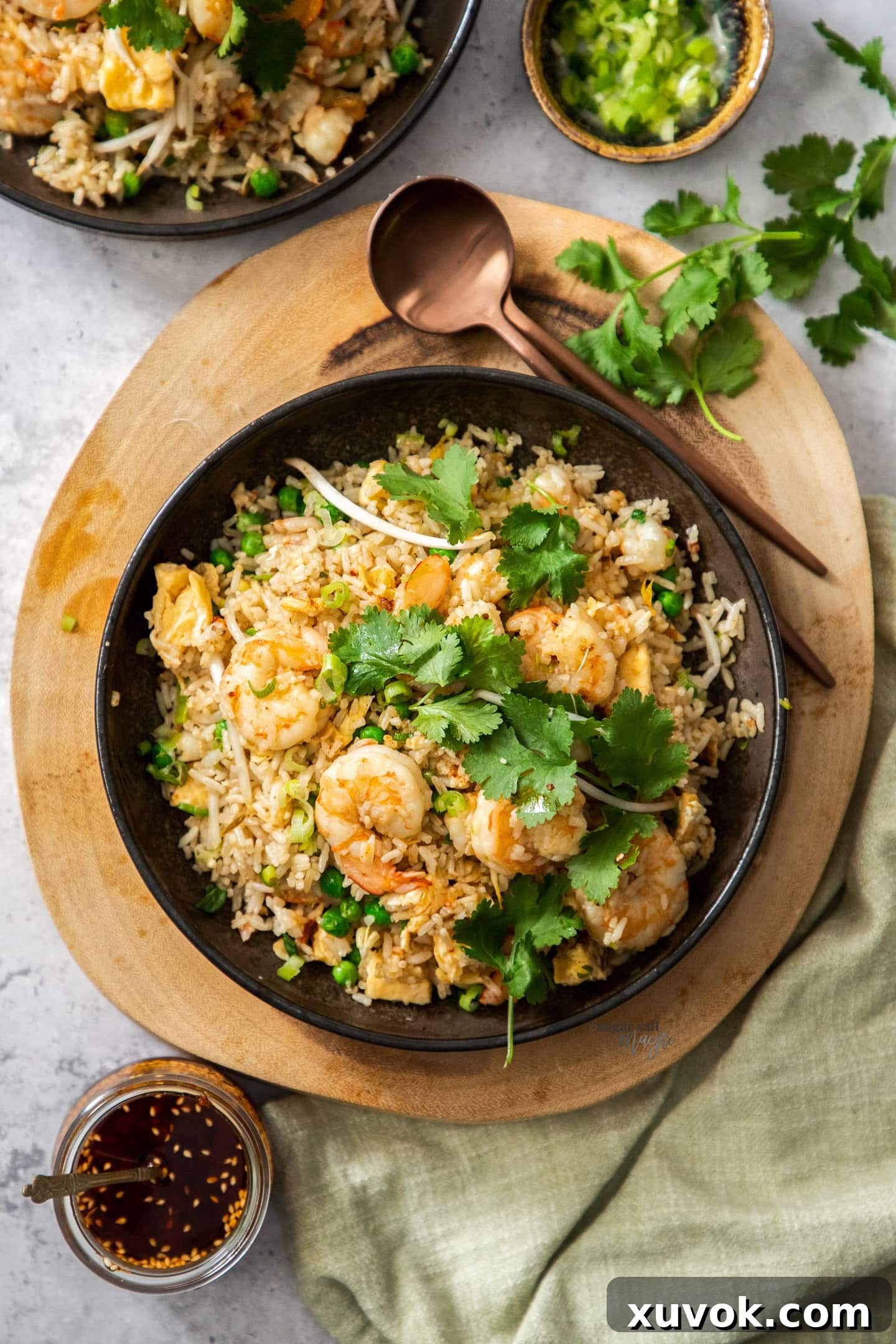 Top down view of a bowl of prawn fried rice on a wooden platter with spoons, garnished with fresh coriander.