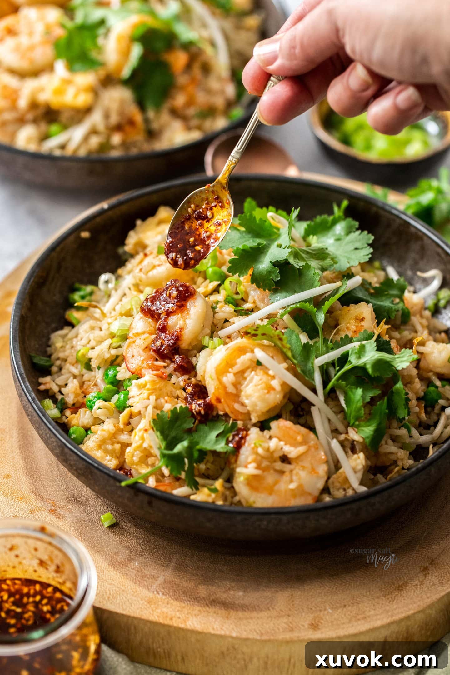 Chilli oil being drizzled from a spoon over a bowl of freshly cooked prawn fried rice.