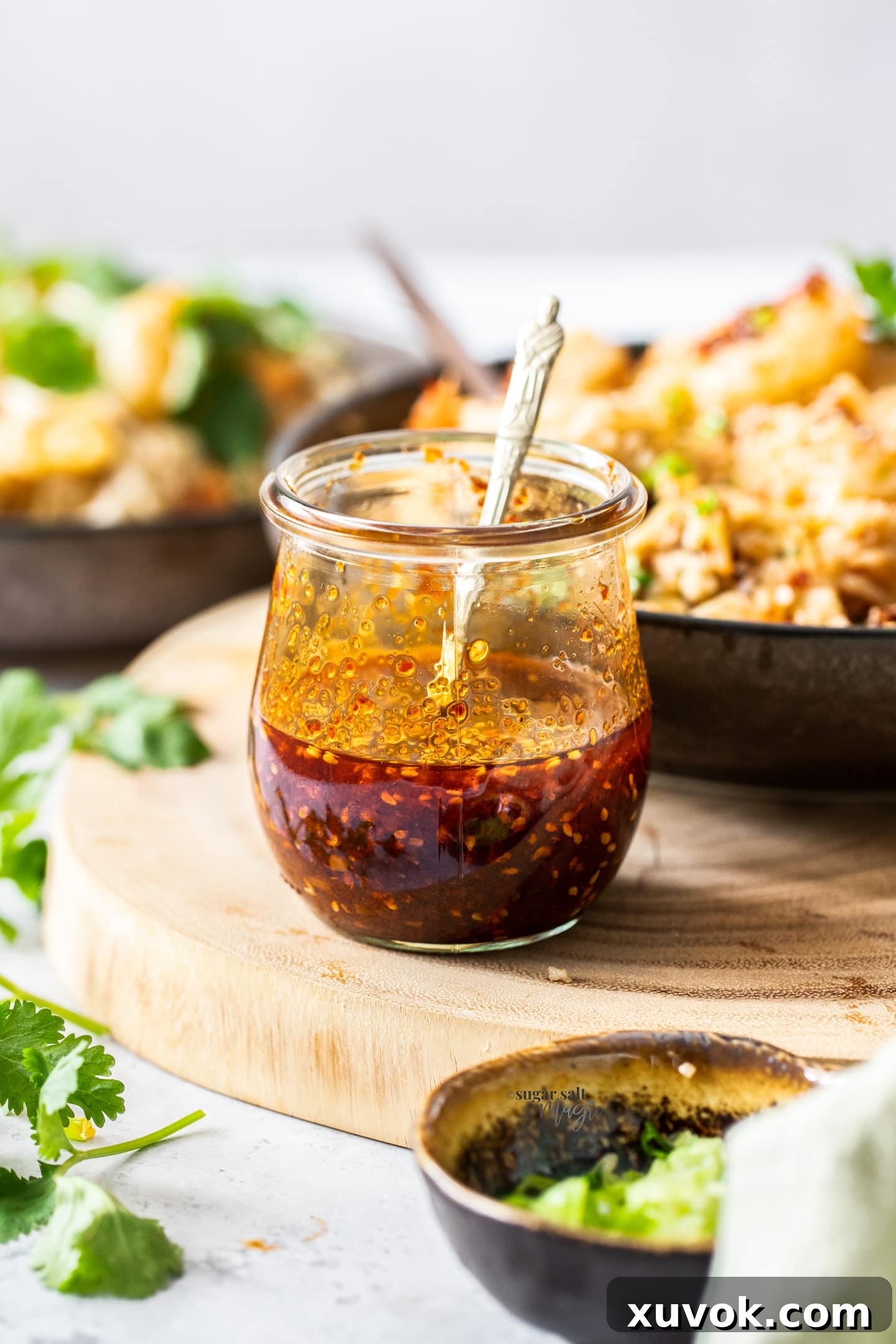 A small glass jar filled with vibrant red chilli oil, garnished with sesame seeds.