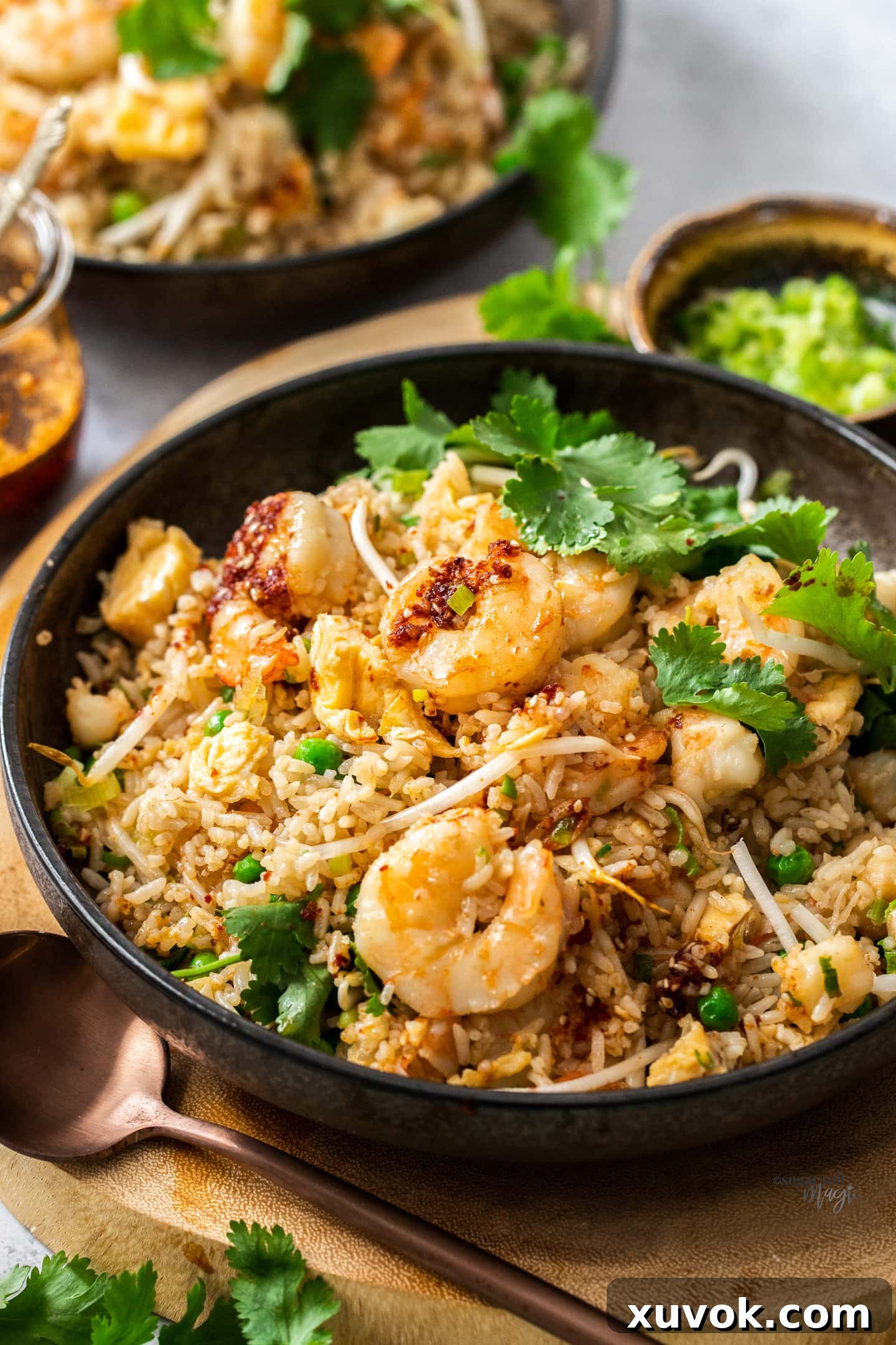A beautifully presented bowl of prawn fried rice with a spoon resting in front, garnished with fresh herbs.