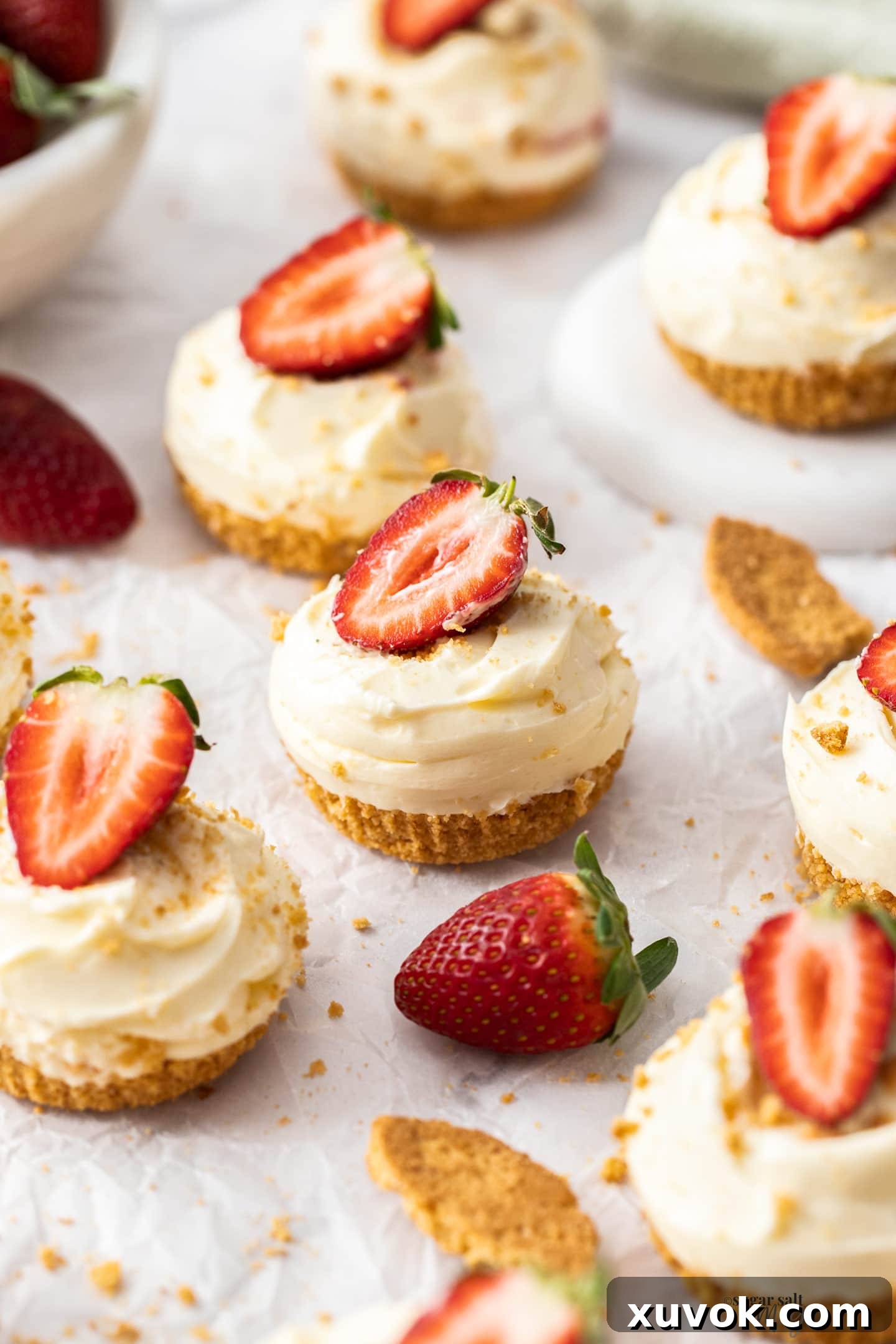 A beautiful batch of no-bake mini strawberry cheesecakes, perfectly arranged on baking paper, ready to be enjoyed.