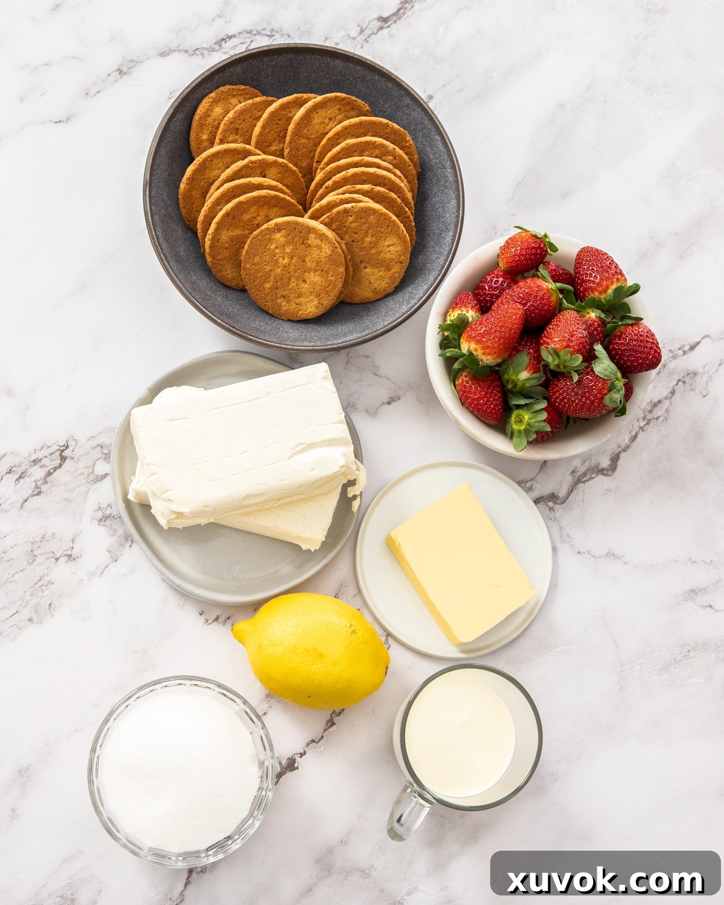 All the fresh and pantry ingredients laid out on a marble countertop for making easy mini strawberry cheesecakes.