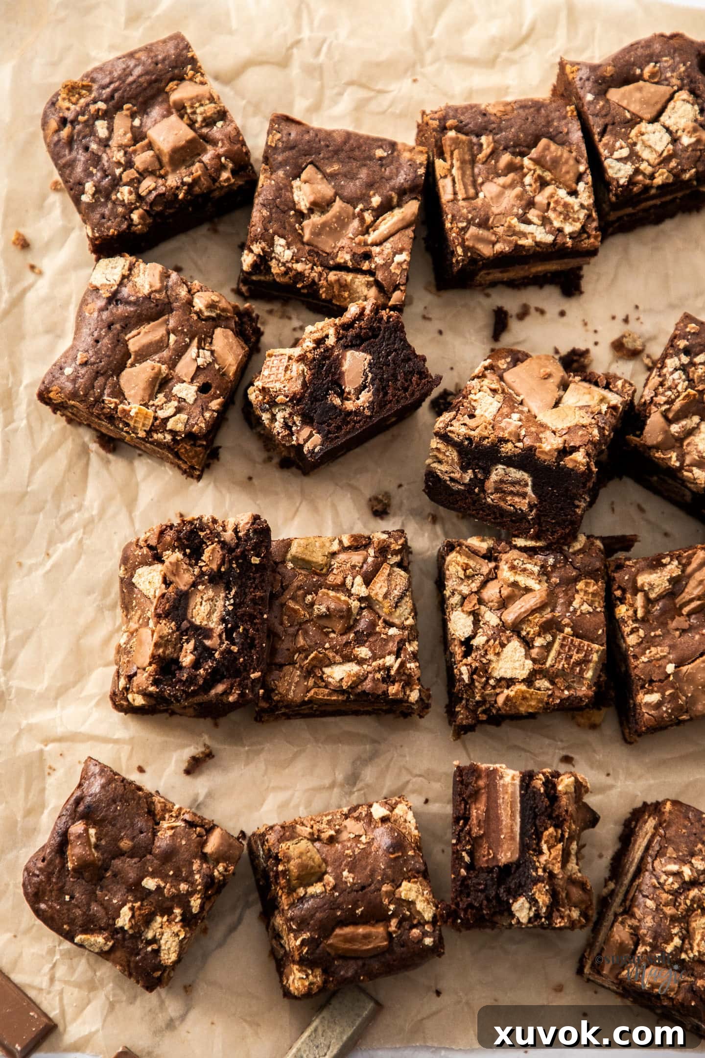Top down view of a batch of 16 fudgy Kit Kat brownies on a sheet of baking paper, showcasing their rich chocolate color and Kit Kat chunks.