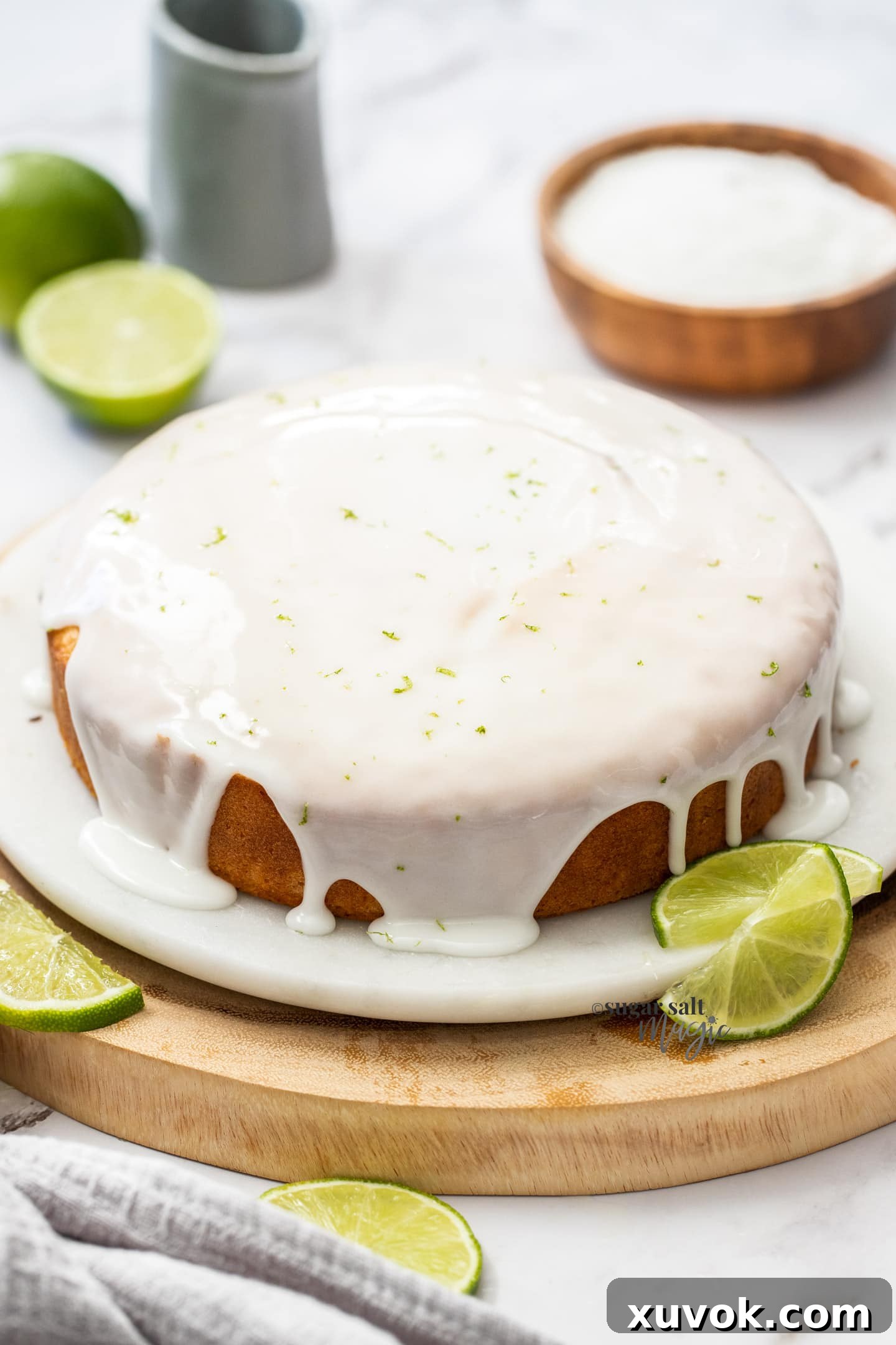 A whole lime and coconut cake, beautifully coated with a glistening lime glaze, resting on a white marble cake stand.