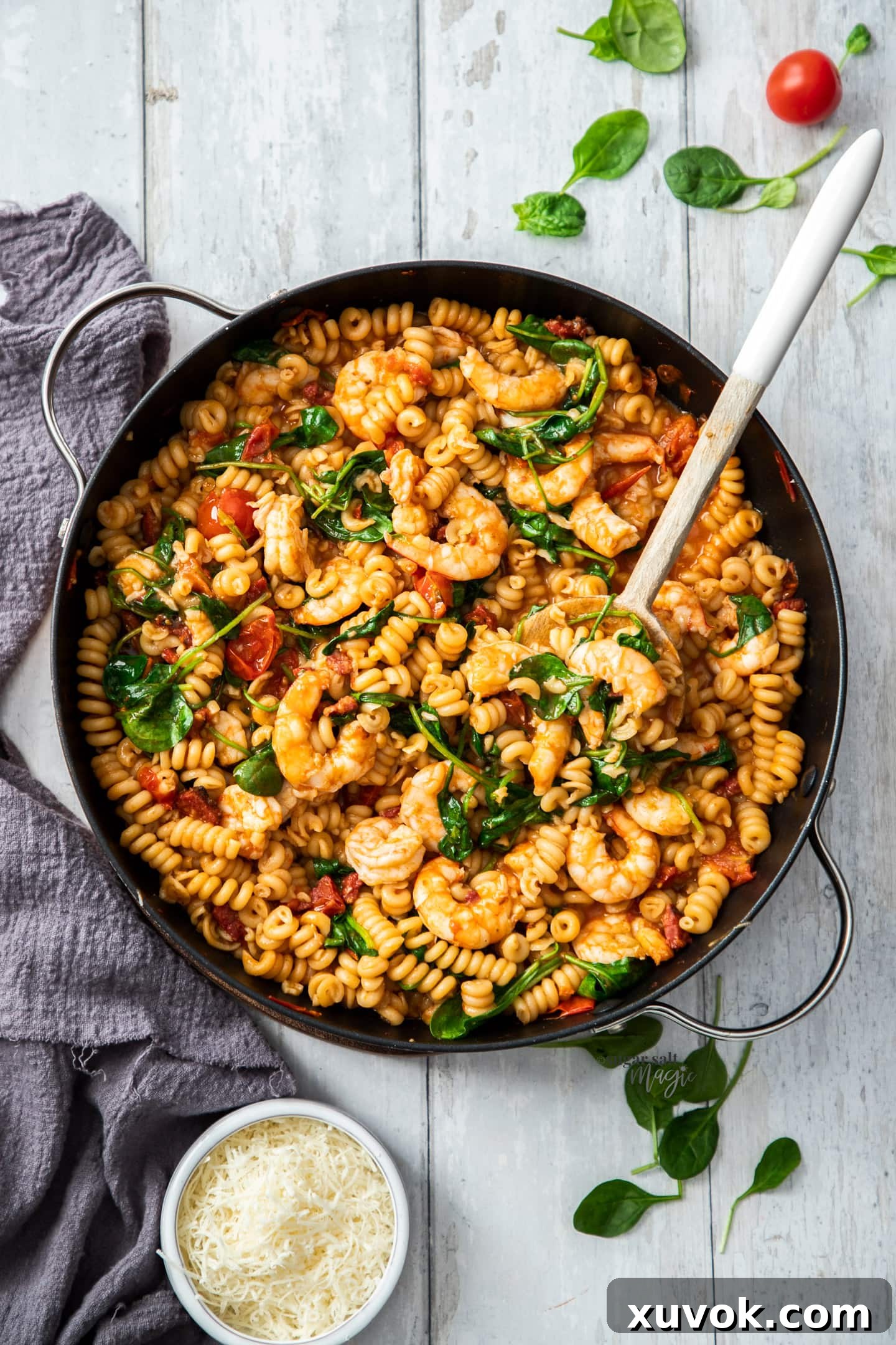 Top down view of prawns in pasta in a large skillet, garnished with fresh herbs.