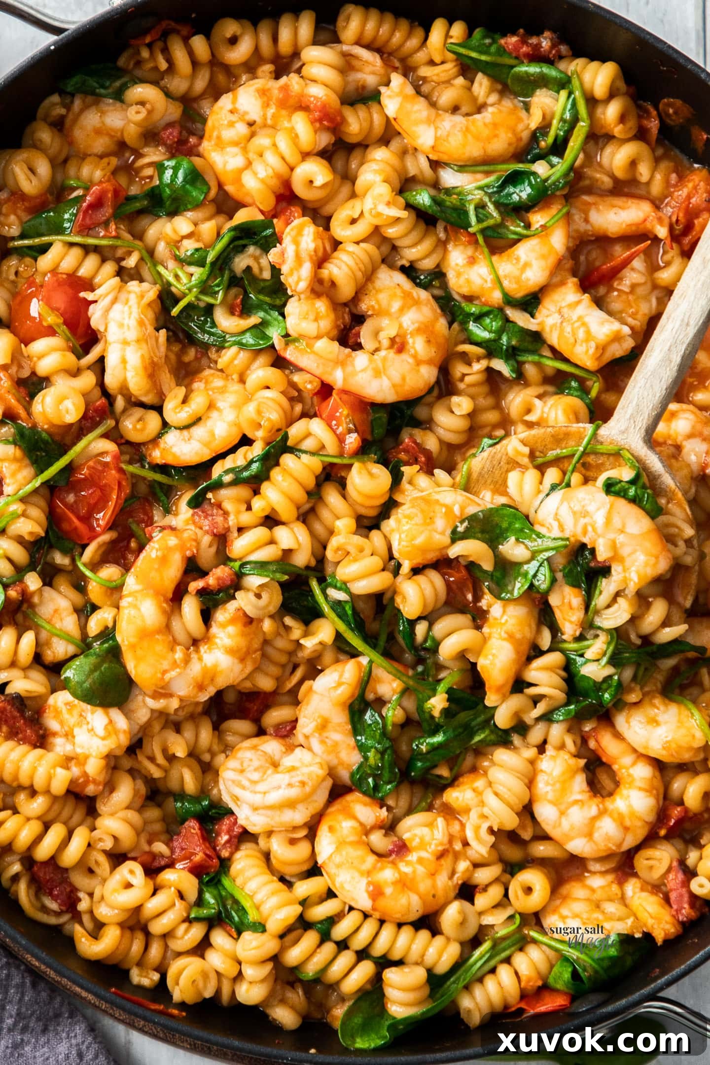 Closeup view of a rich prawn and chorizo pasta dish, with wilted spinach, in a large skillet, ready to be served.