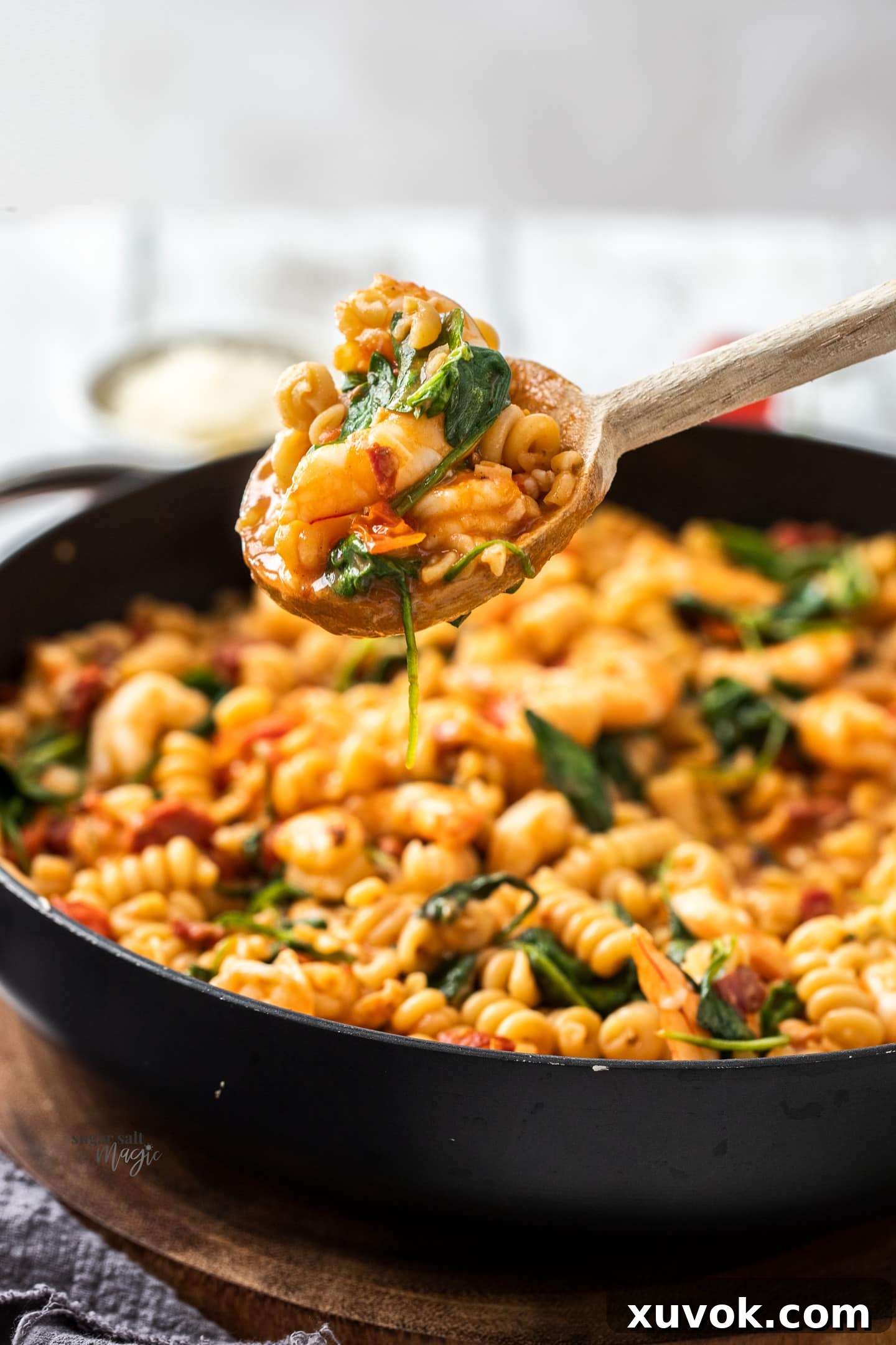 A wooden spoon carefully scooping a generous portion of prawn and chorizo pasta from a steaming skillet.