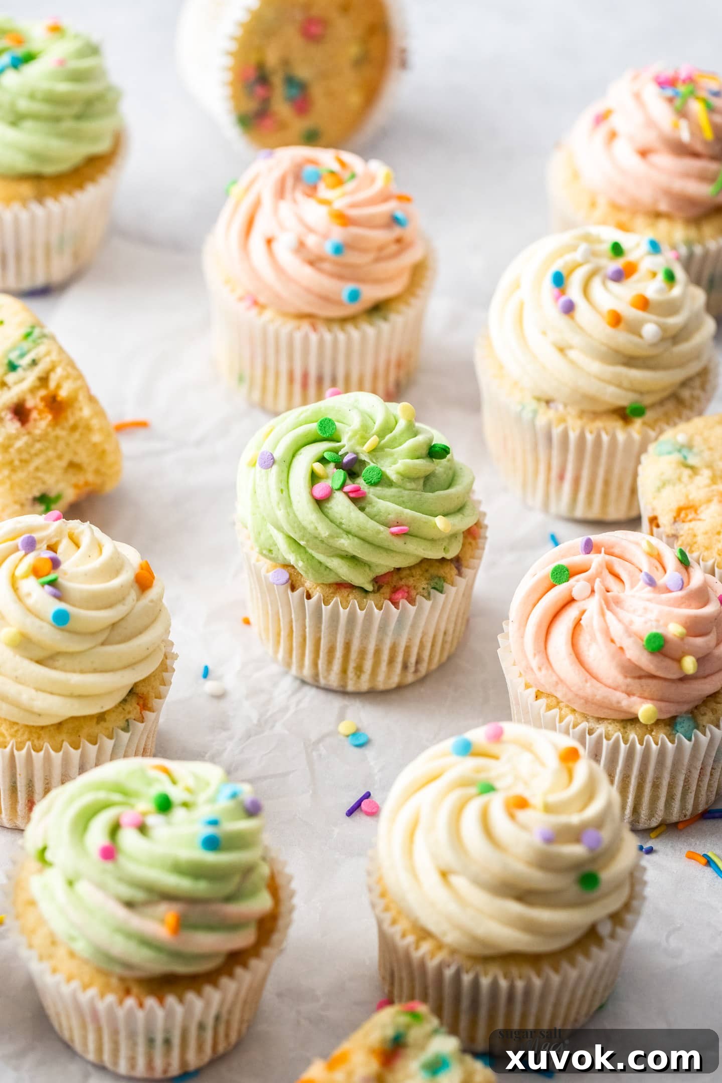 A batch of 12 confetti cupcakes, some with different colored frosting, arranged on a cooling rack.