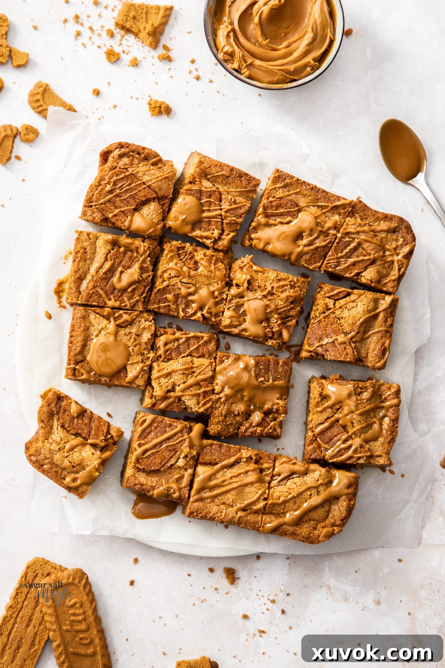 A top-down view of a batch of neatly sliced Biscoff blondie squares arranged on a platter, with a small jar of Biscoff spread positioned beside them.