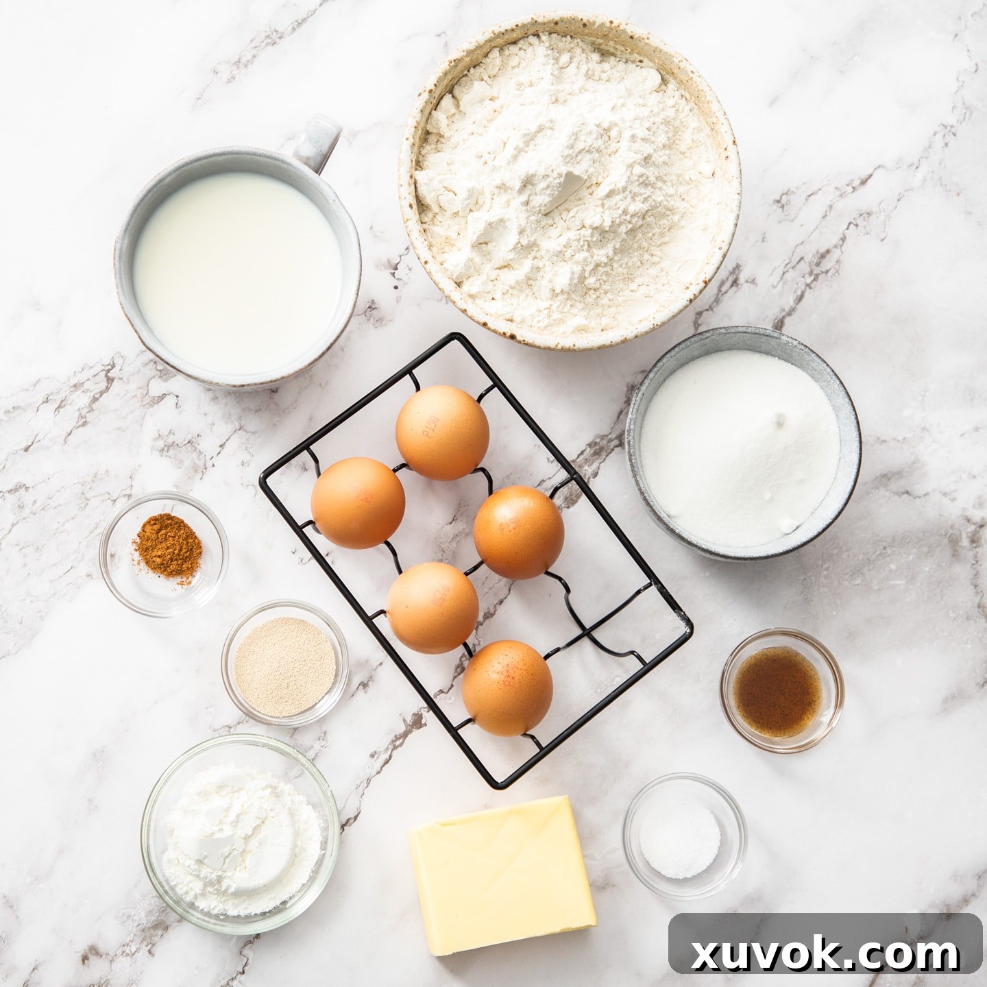 A curated selection of fresh ingredients for Bavarian Cream Donuts, including flour, eggs, milk, sugar, butter, and vanilla, neatly arranged on a marble surface.