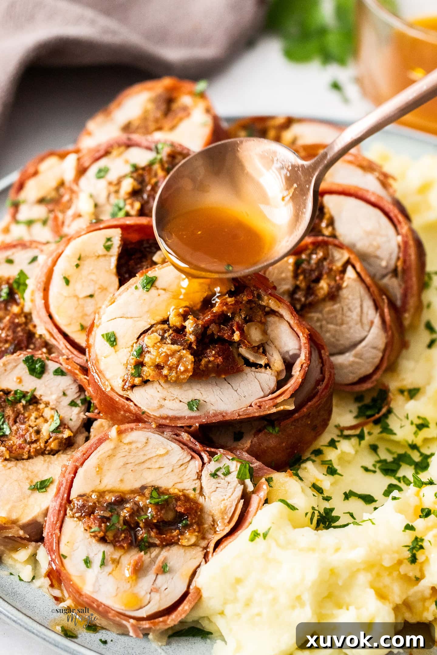 A perfectly cooked slice of prosciutto-wrapped stuffed pork tenderloin with a rich pan sauce being spooned over.