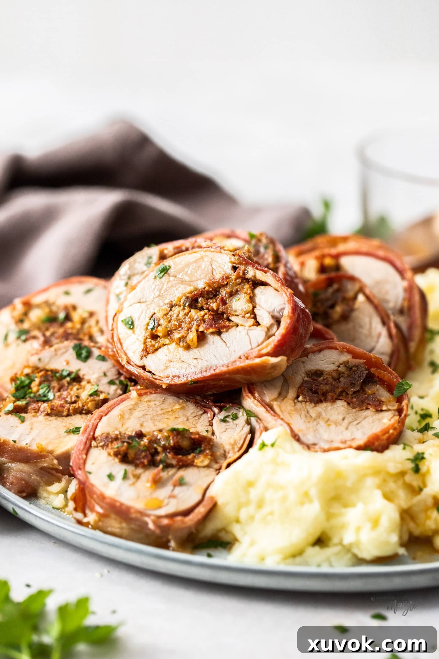 A close-up view of a slice of perfectly cooked stuffed pork tenderloin, showcasing the vibrant sundried tomato pesto filling and the crispy prosciutto wrap.