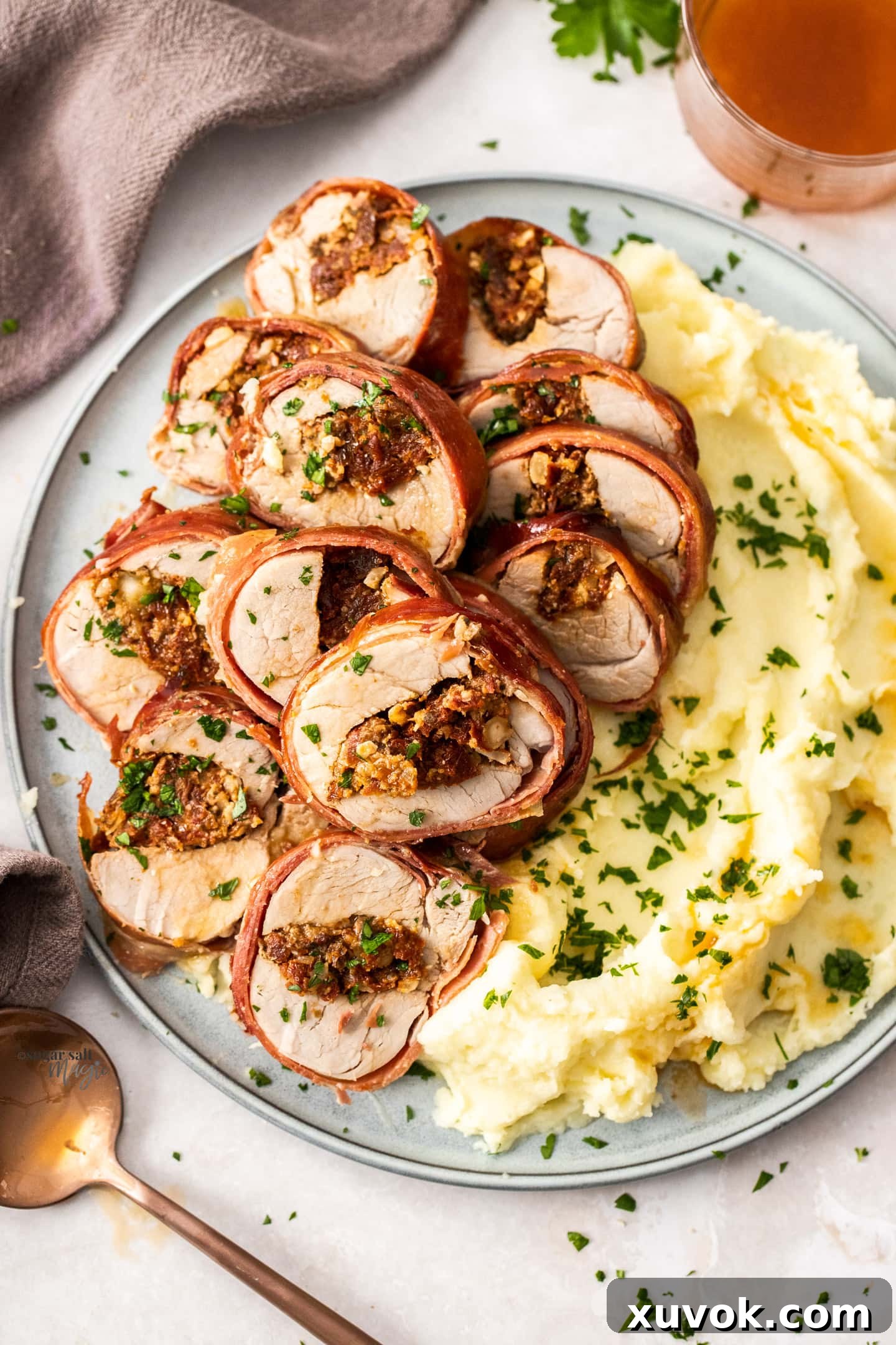 A beautifully presented serving platter with slices of stuffed pork tenderloin nestled beside a generous portion of fluffy potato mash.