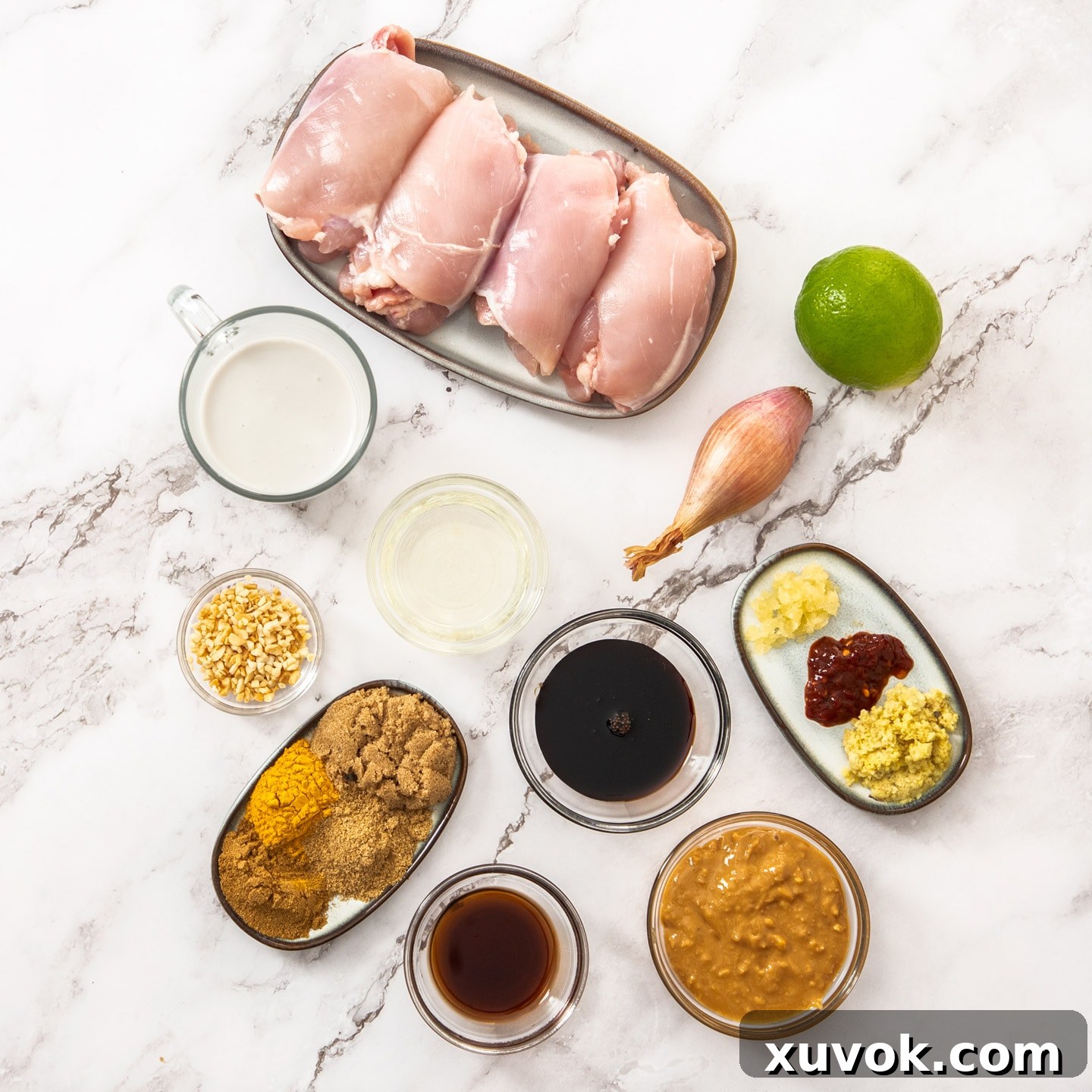 A vibrant selection of fresh ingredients for Thai chicken satay laid out on a clean marble countertop.