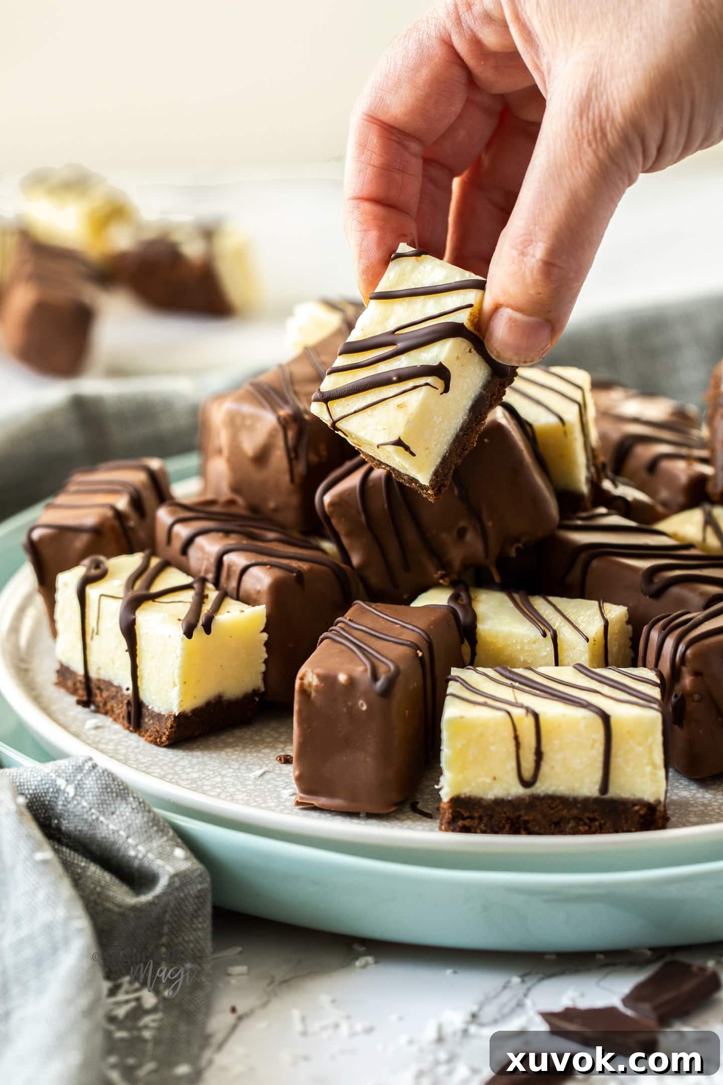A hand reaching for a piece of chocolate-coated coconut fudge bar from a white plate.