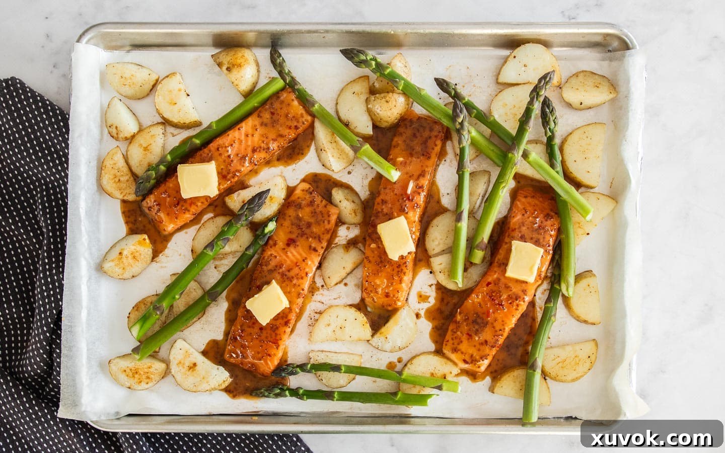 The salmon fillets topped with butter and surrounded by asparagus, ready to bake.
