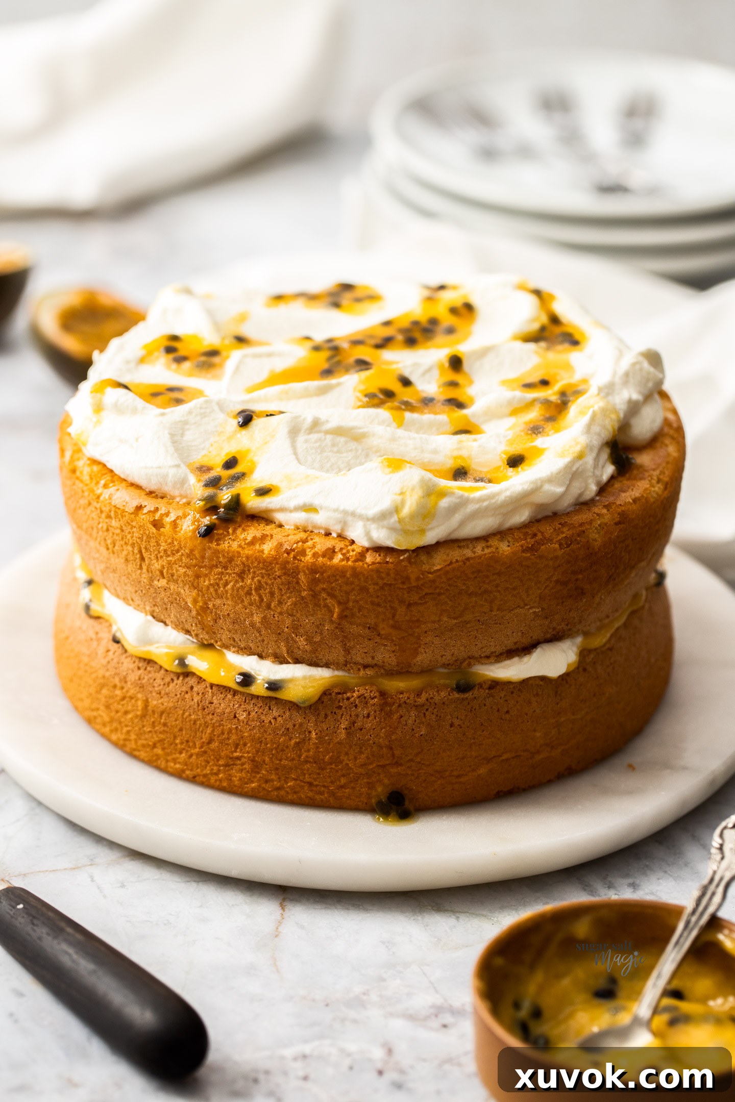 Passionfruit sponge cake sitting on a marble cake plate, adorned with fresh passionfruit pulp.