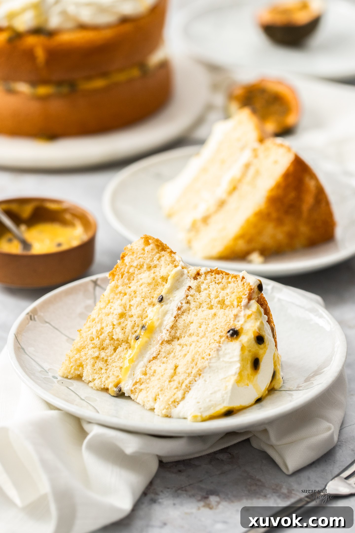 Slices of sponge cake on dessert plates with a bowl of passionfruit curd, showcasing the light texture.