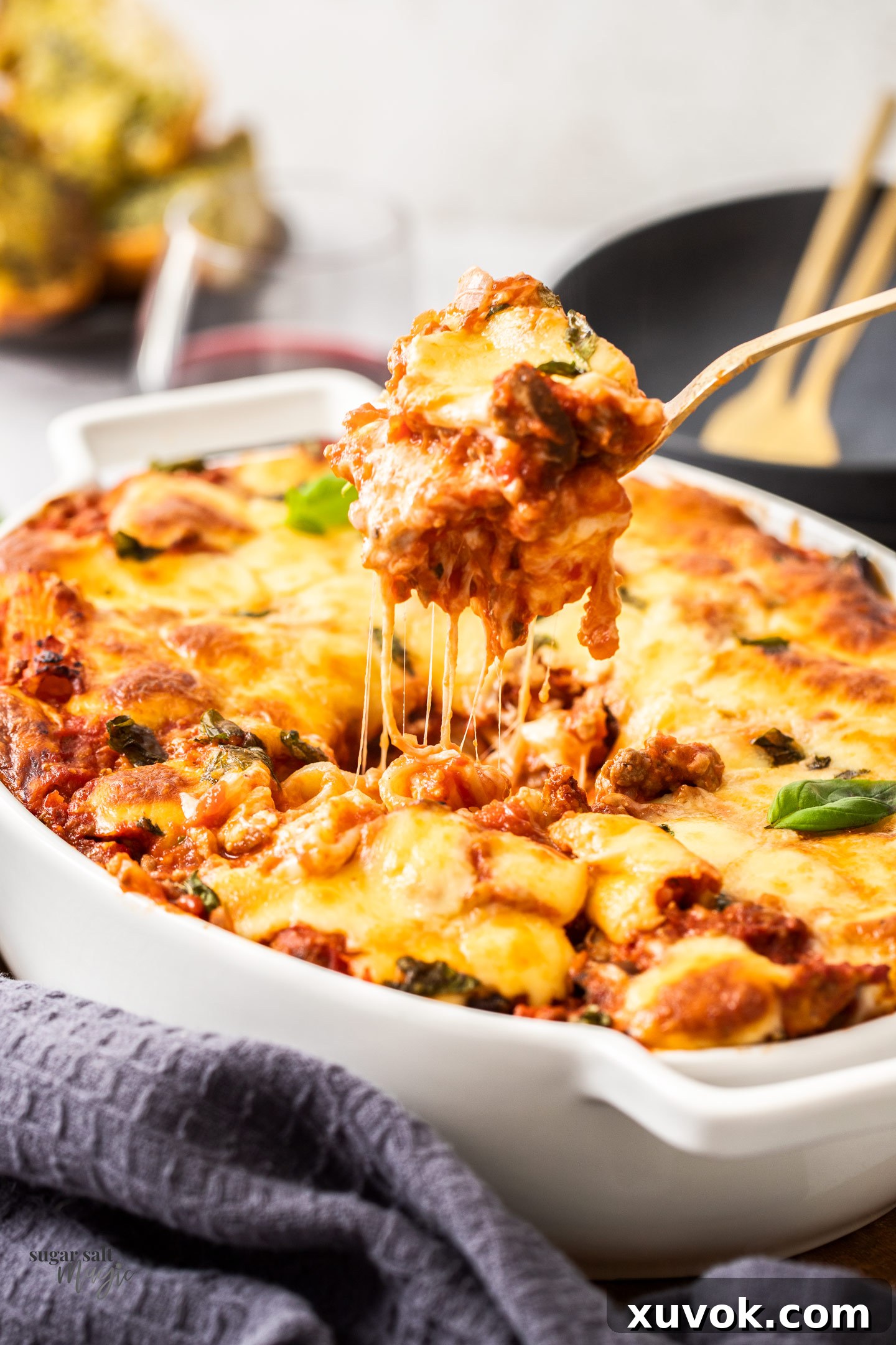 A serving spoon scooping out a generous portion of rigatoni al forno from a casserole dish, revealing the saucy pasta and melted cheese inside.