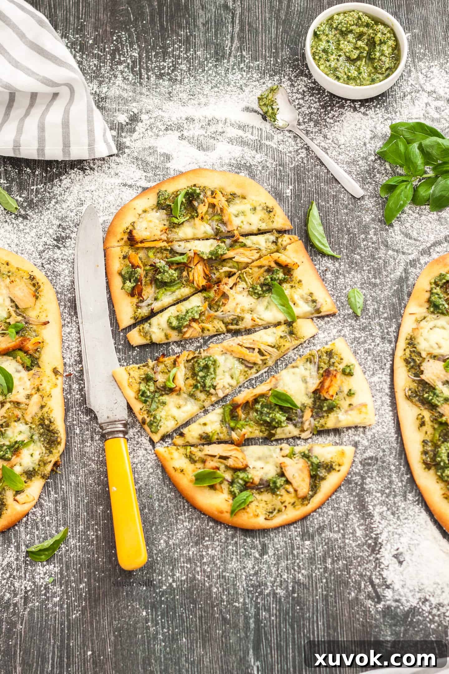 Three flatbreads topped with vibrant pesto, tender shredded turkey, and melted cheese, expertly cut into slices and arranged on a rustic wooden surface.