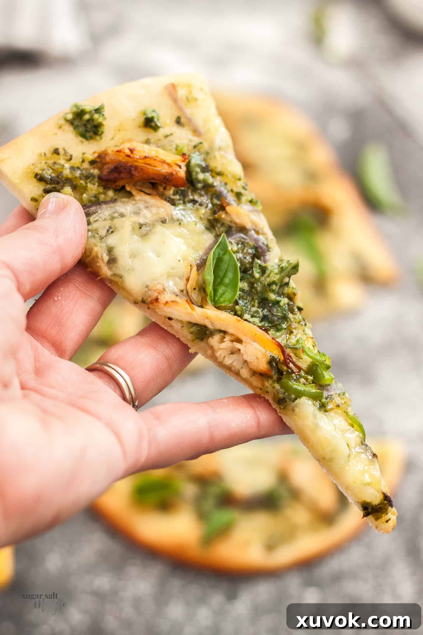 A hand reaching for a freshly baked slice of pesto turkey flatbread, showcasing its crispy crust and melted cheese.