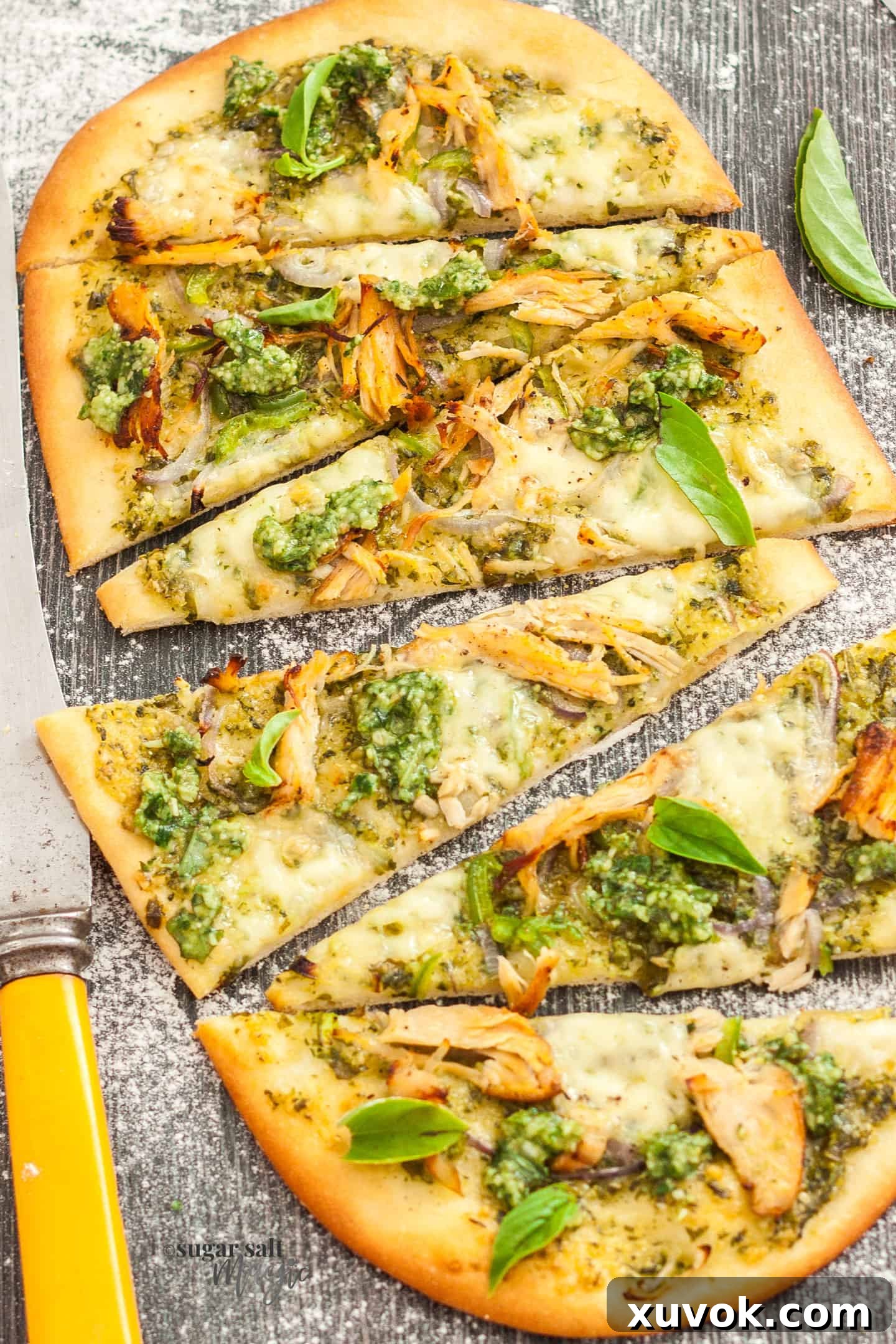A vibrant pesto turkey flatbread, perfectly baked with melted cheese and fresh toppings, sliced and ready to serve on a wooden board.