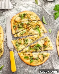 Flatbread topped with pesto and turkey, cut into slices, on a wood surface.