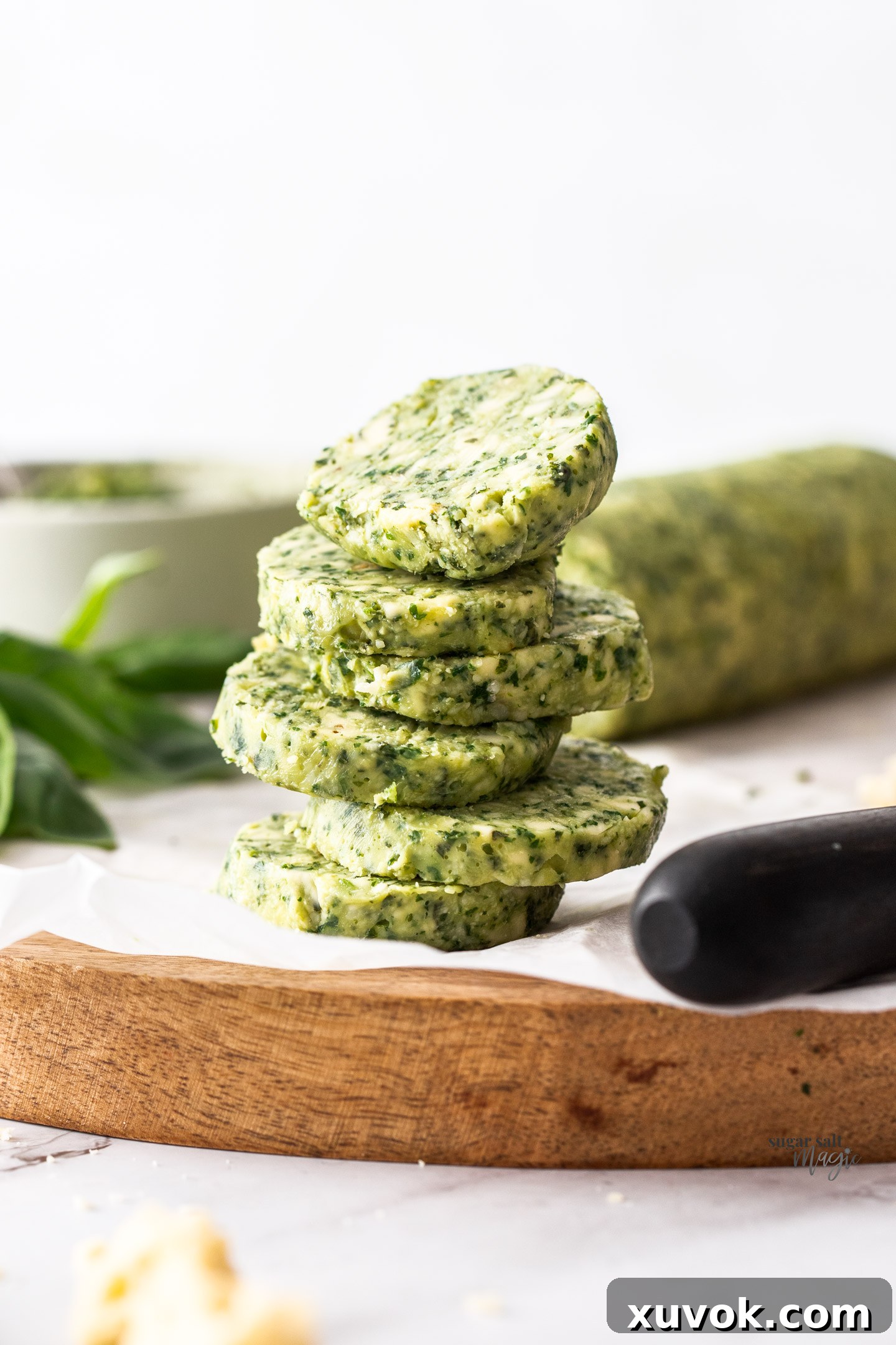 A stack of six perfectly cut disks of basil pesto butter, vibrant green and ready to melt into your favorite dishes.