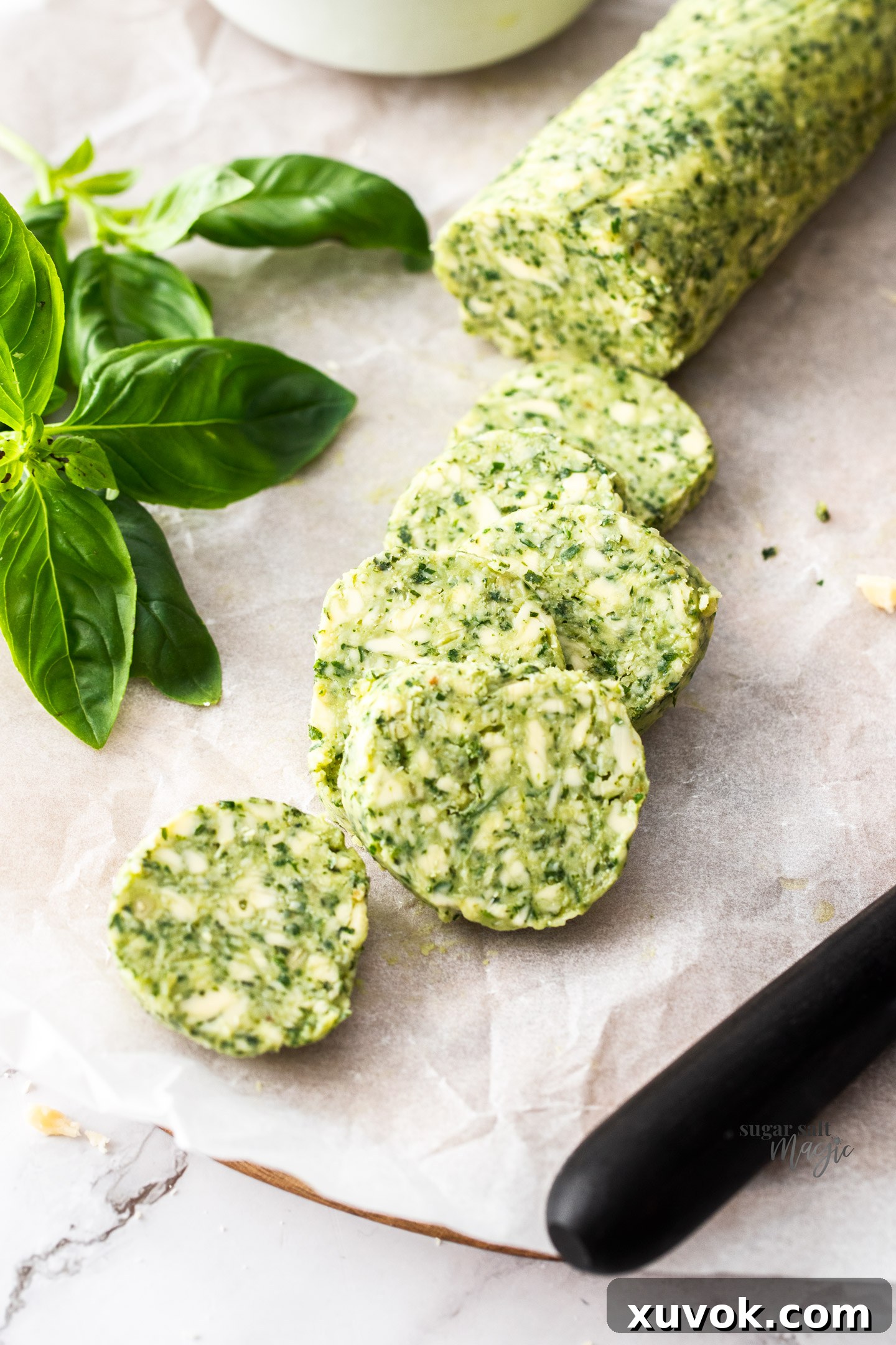 Fresh basil leaves artfully placed next to neat disks of vibrant green pesto butter, highlighting the key ingredient.