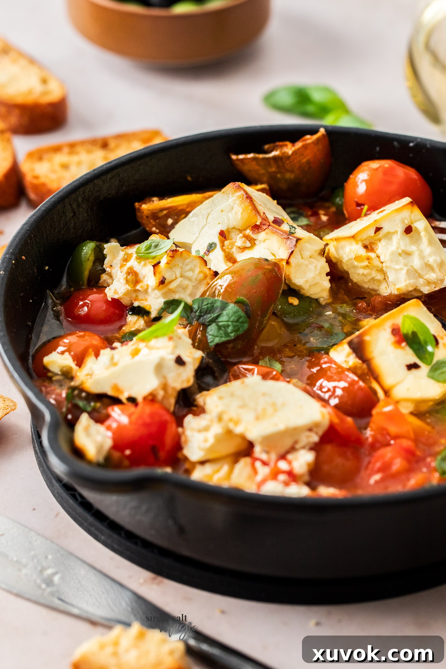 Close up of roasted tomatoes and feta in a cast iron skillet, showcasing the creamy texture and vibrant colors.