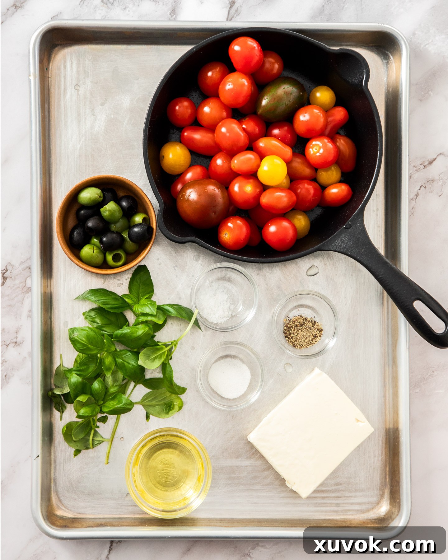 Ingredients for baked feta and tomatoes arranged neatly on a metal tray, ready for preparation.