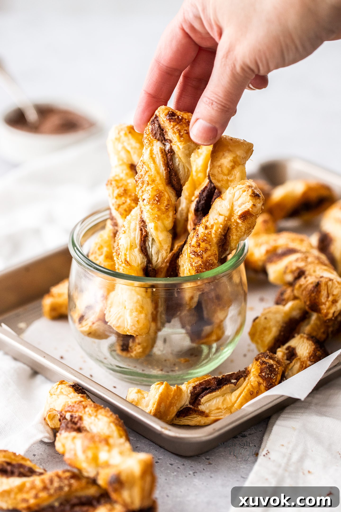 Nutella puff pastry twists standing upright in a clear glass jar, ready to be enjoyed.