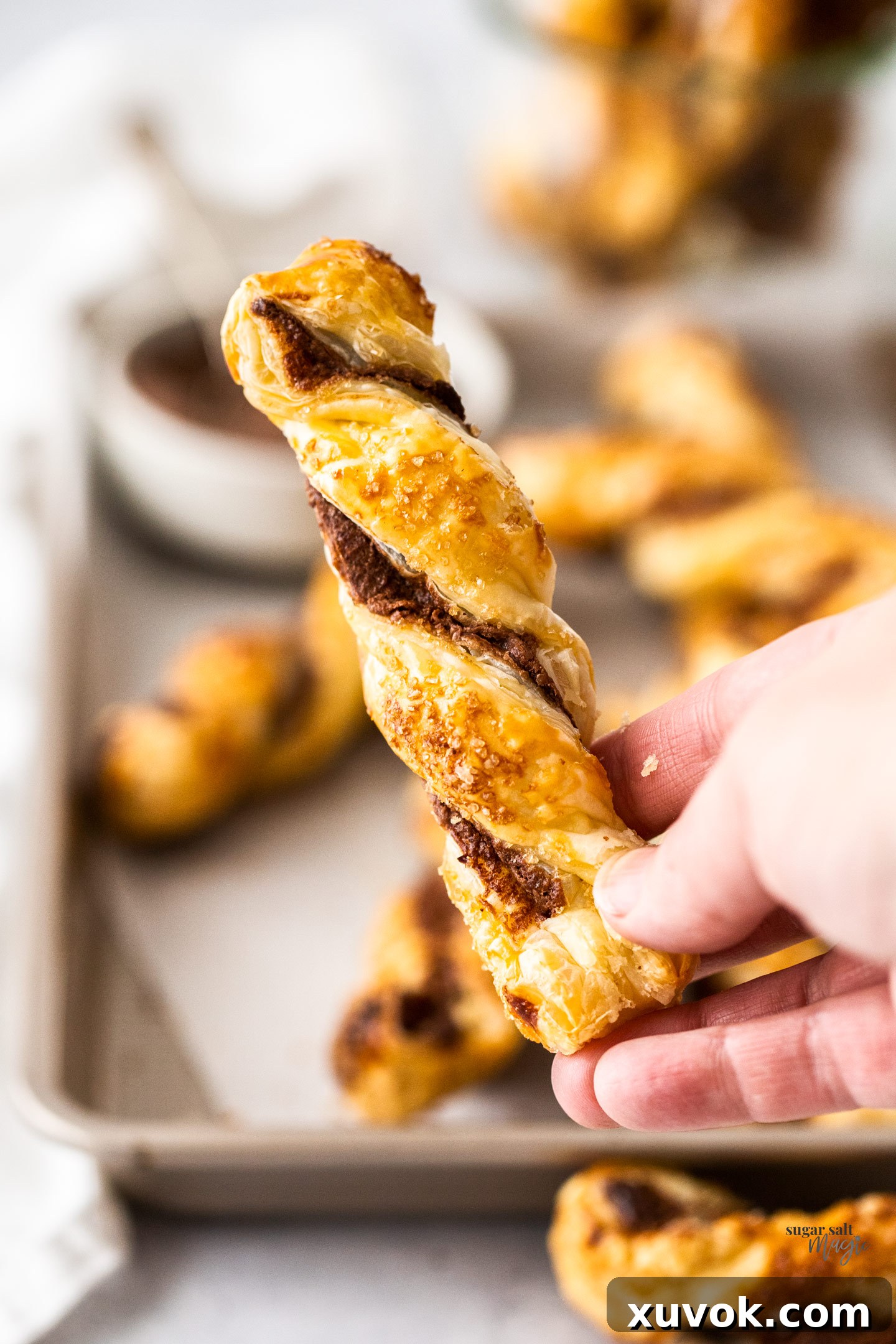 A hand reaching for a golden-brown Nutella twist, highlighting its tempting texture.