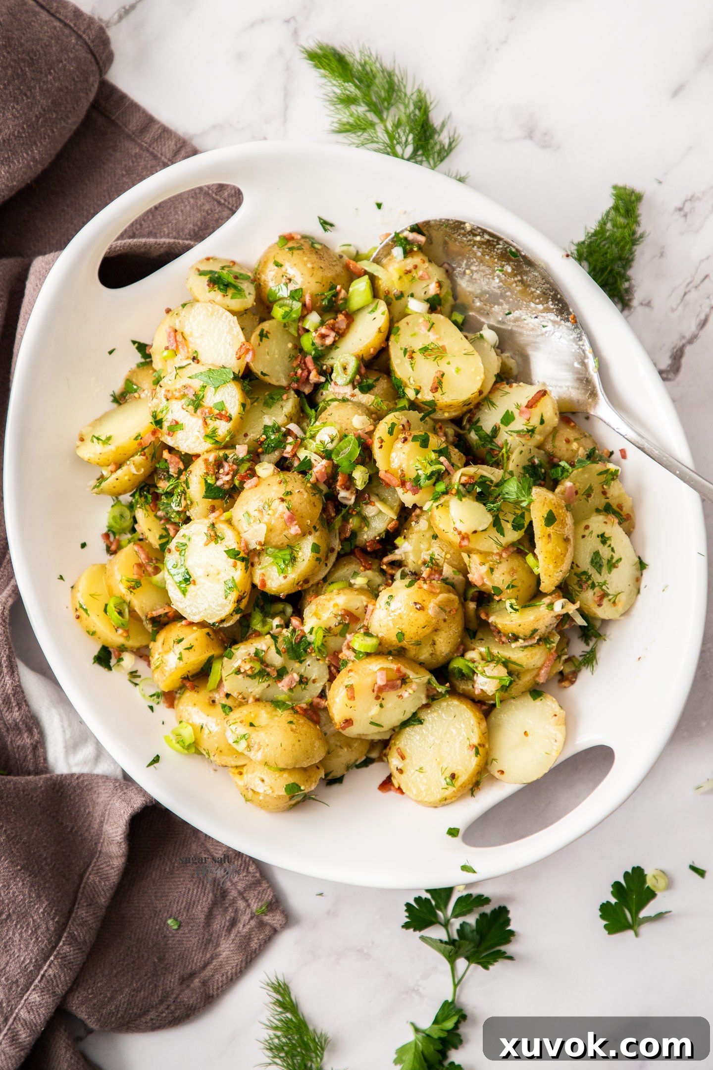 A white bowl filled with vibrant no-mayo potato salad, garnished with fresh herbs.