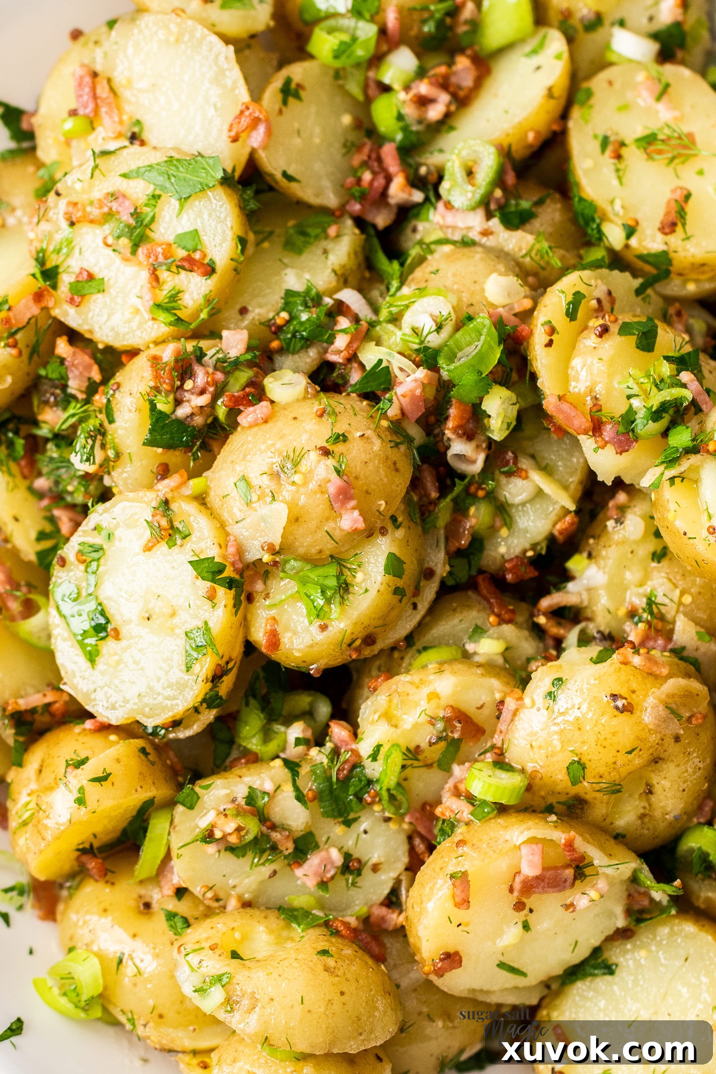 A close-up shot of the vibrant no-mayo potato salad, showing individual potato pieces, crispy bacon, and fresh herbs coated in the zesty dressing.