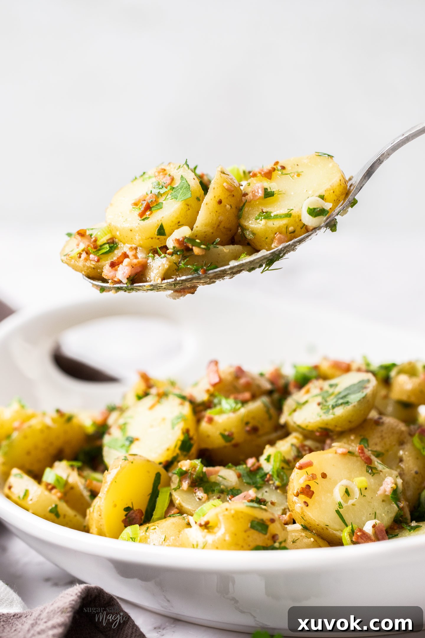 A serving spoon lifting a portion of no-mayo potato salad from a white bowl, showcasing its fresh and vibrant appearance.