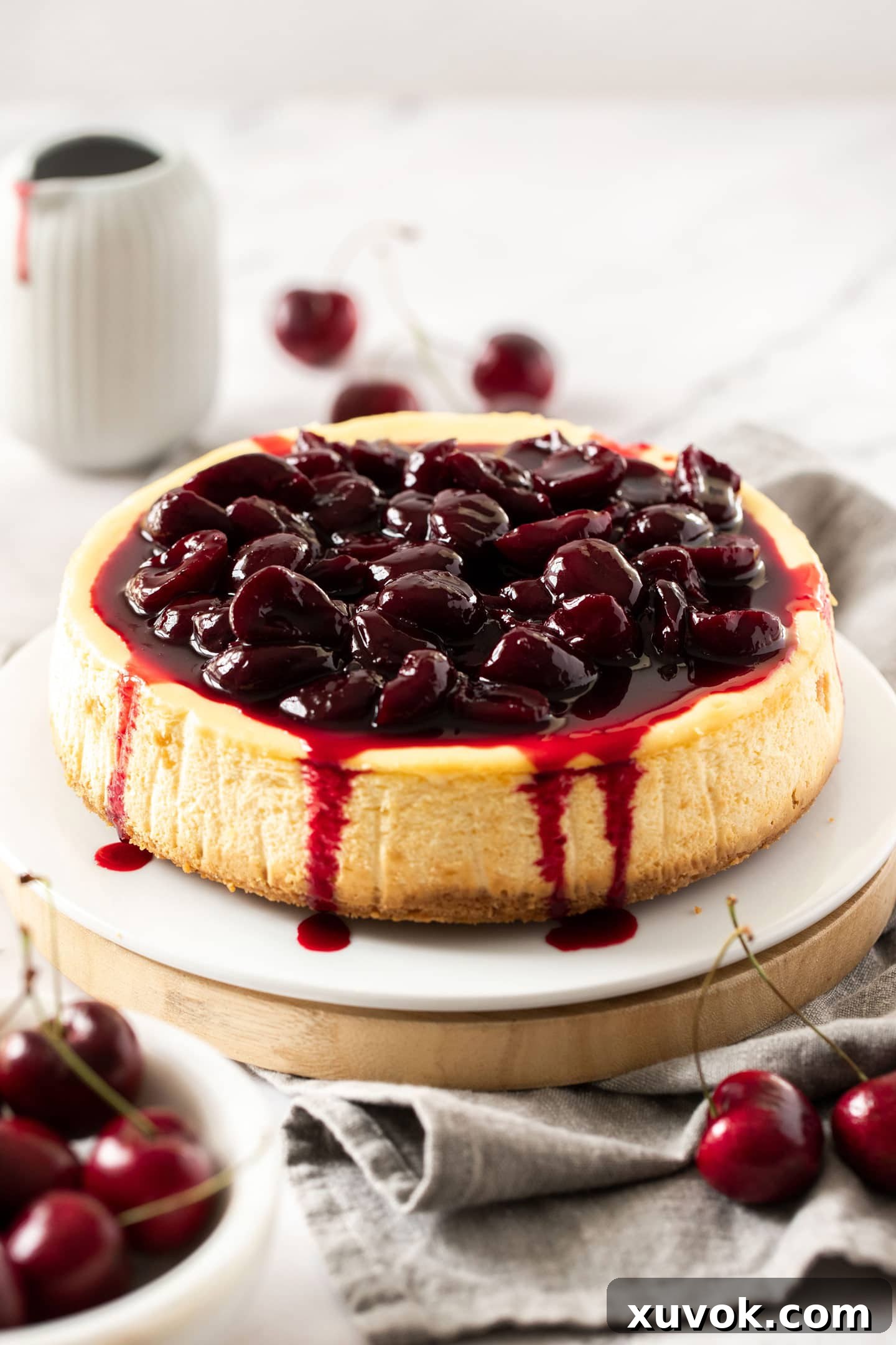 A cheesecake topped with cherry sauce on a white cake plate.